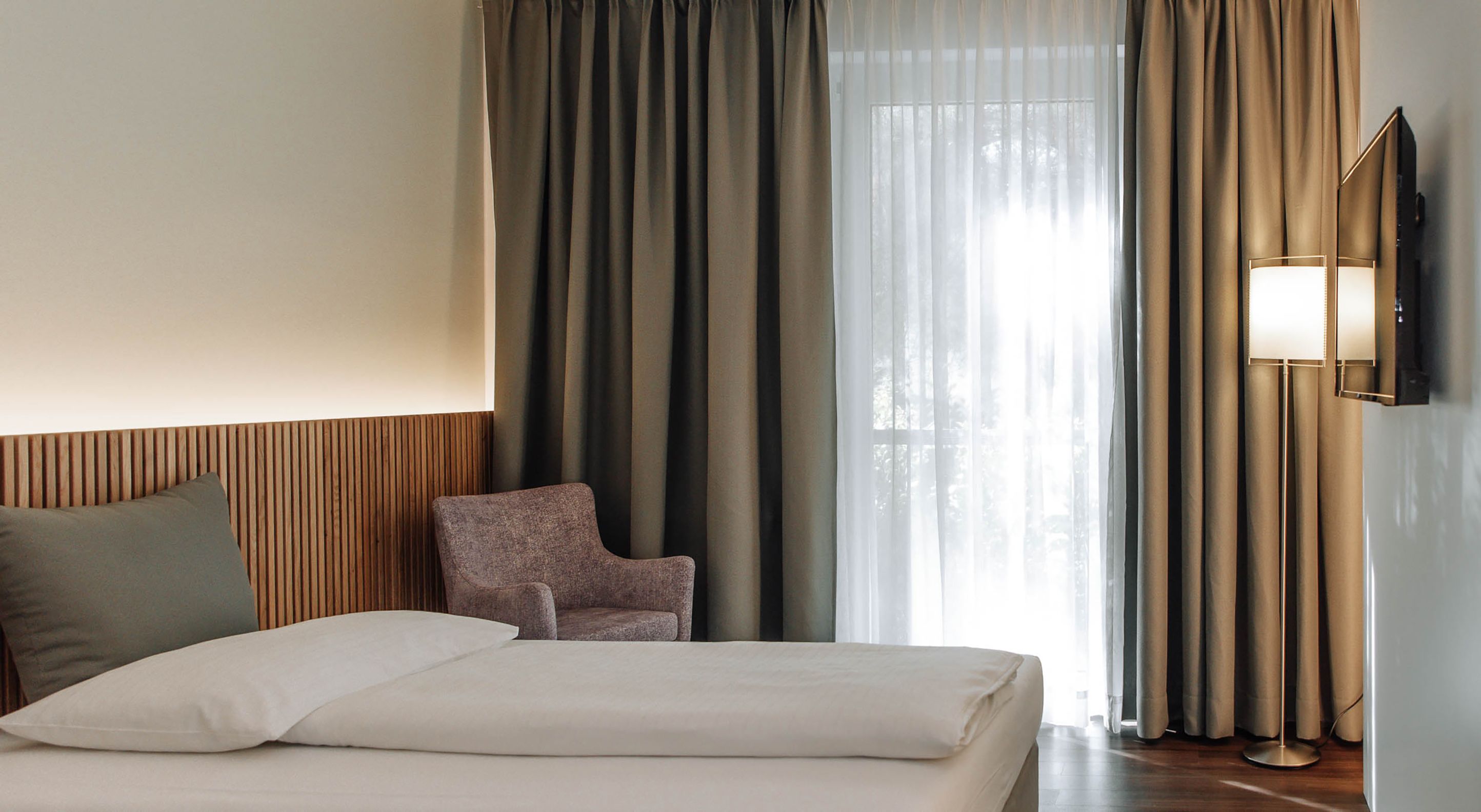 Modern hotel room with bed, armchair and curtains.
