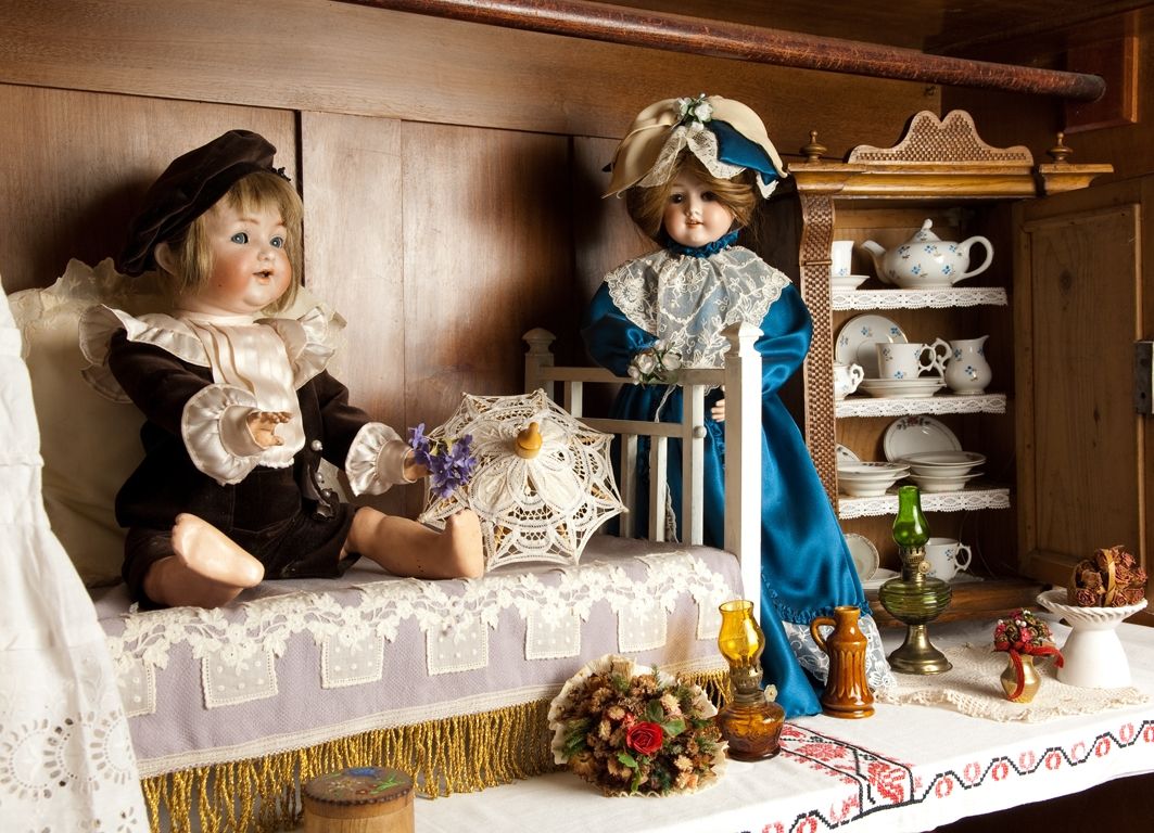 Two antique dolls in a nostalgic room with crockery and decorations.