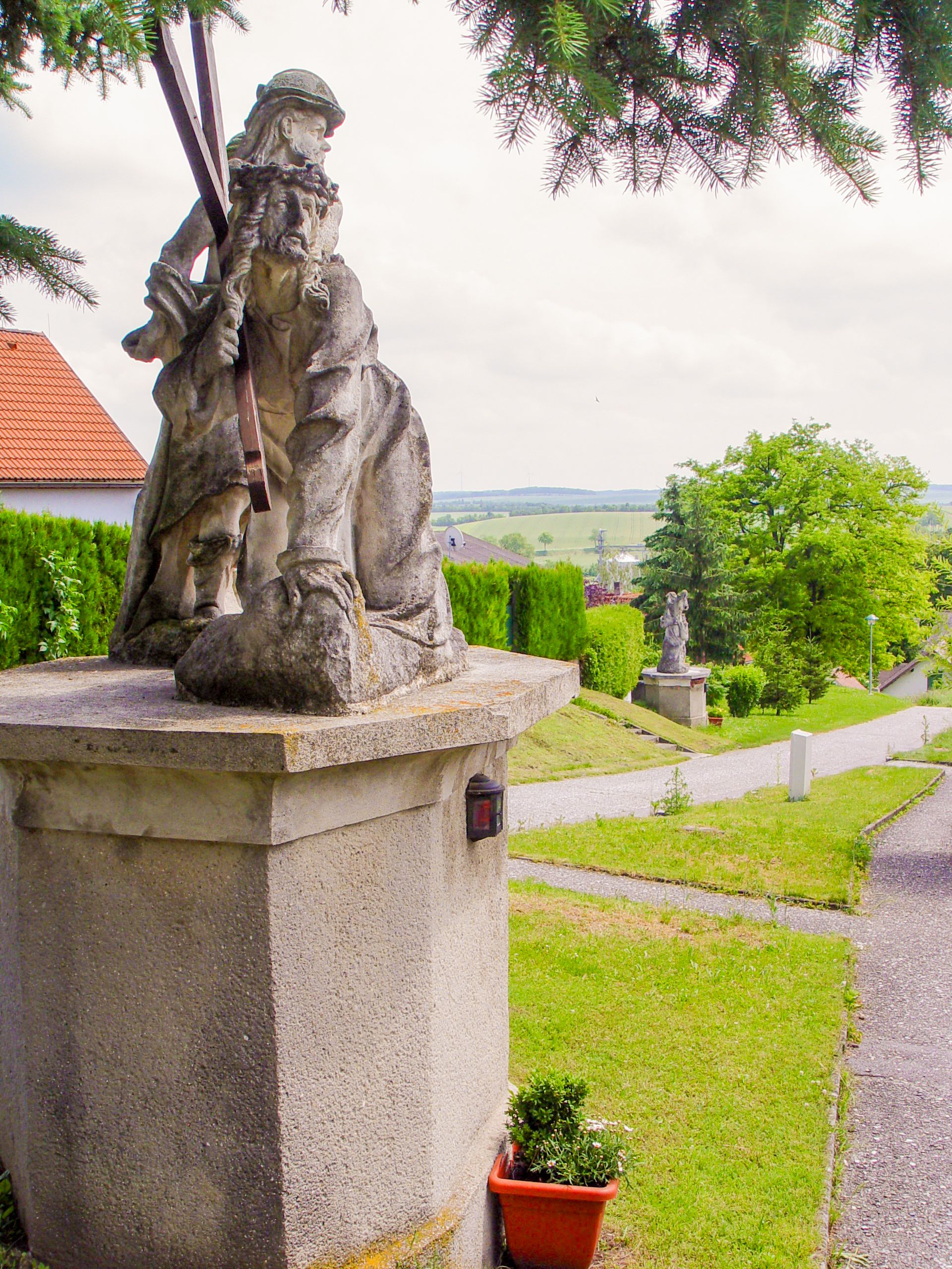 Stone statue on a pedestal with a green landscape in the background.