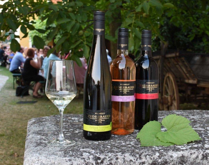 Three bottles of wine and a glass on an outdoor table, with people in the background.