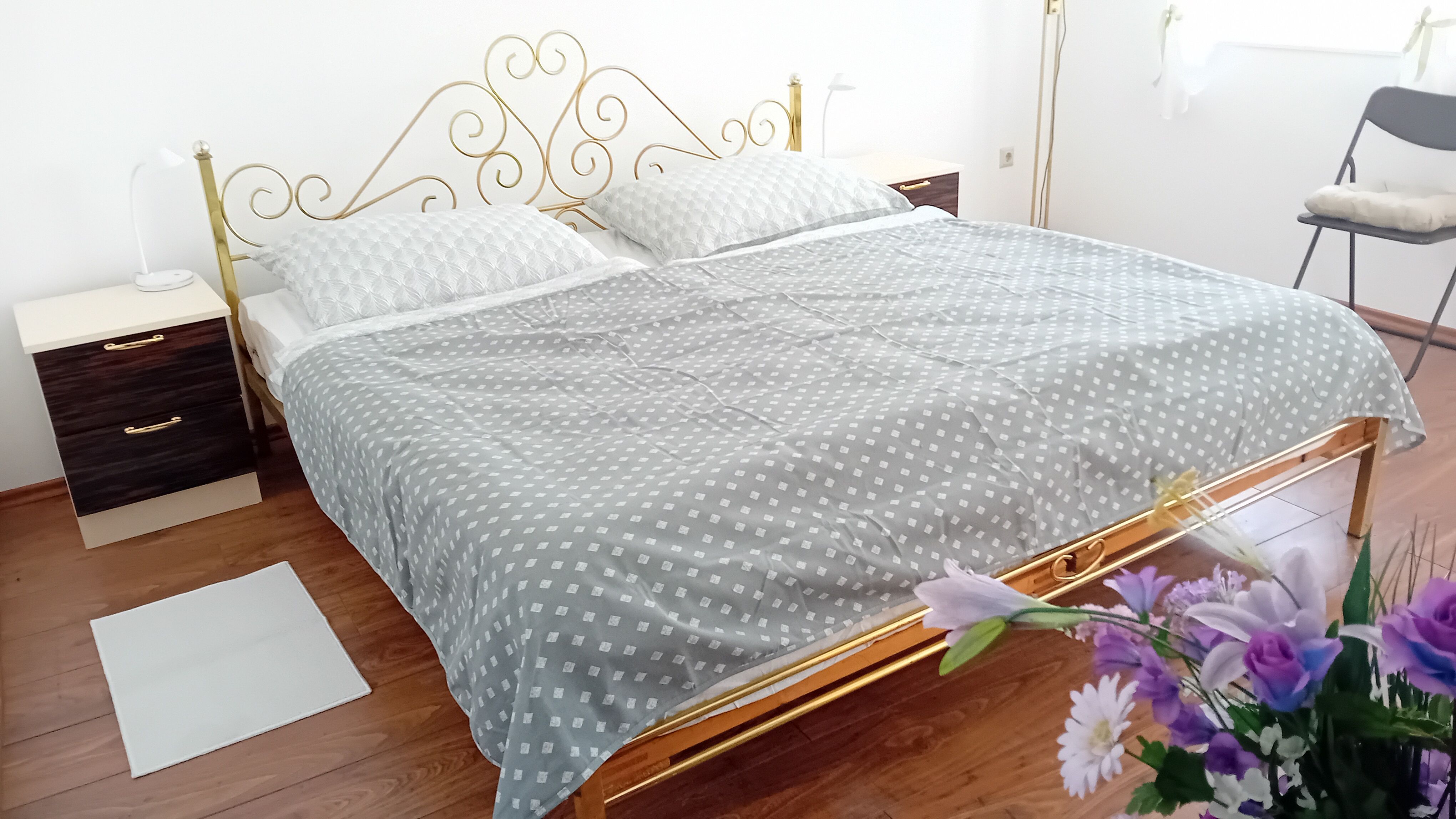 Bedroom with a double bed, gold-colored headboard, two bedside tables and flowers in the foreground.