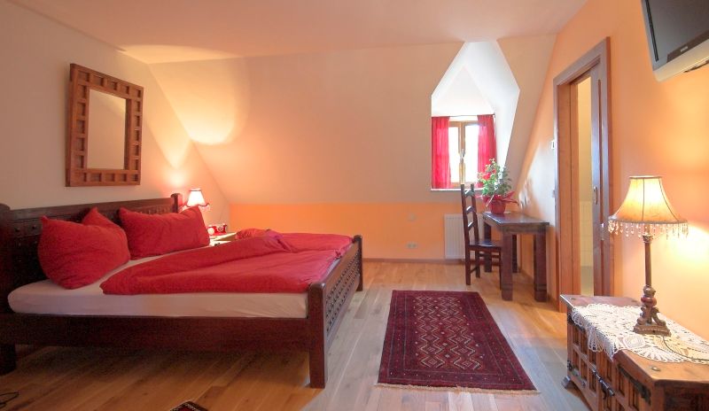 Cozy bedroom with double bed, red bed linen and wooden furniture.