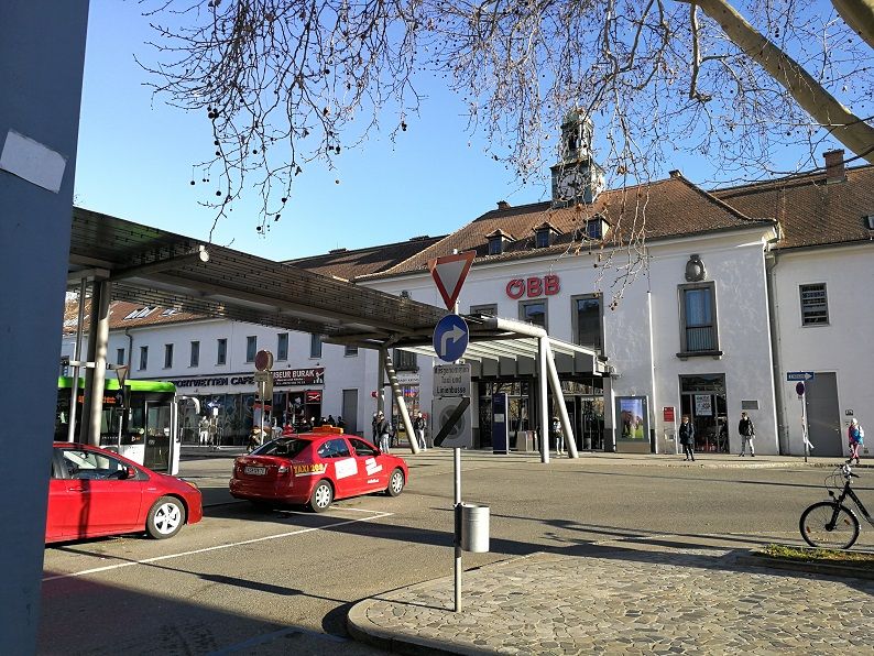 Krems an der Donau station with ÖBB logo, cars and pedestrians.