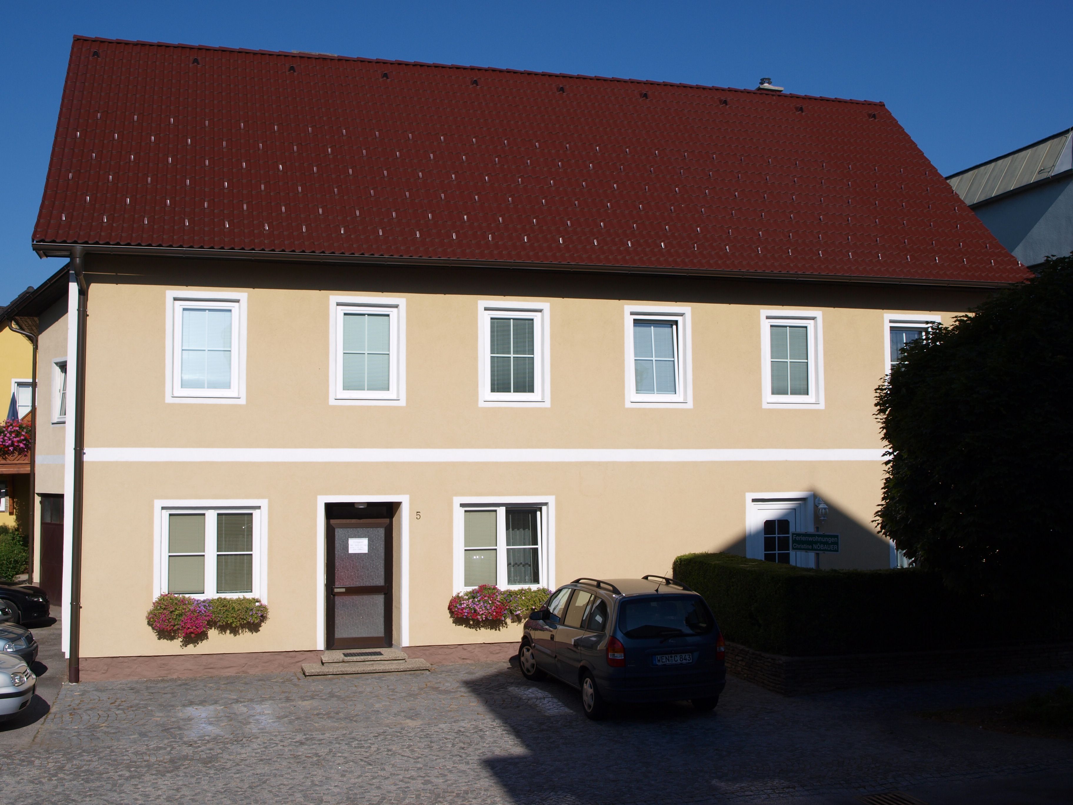 Yellow two-story house with red roof and several windows.