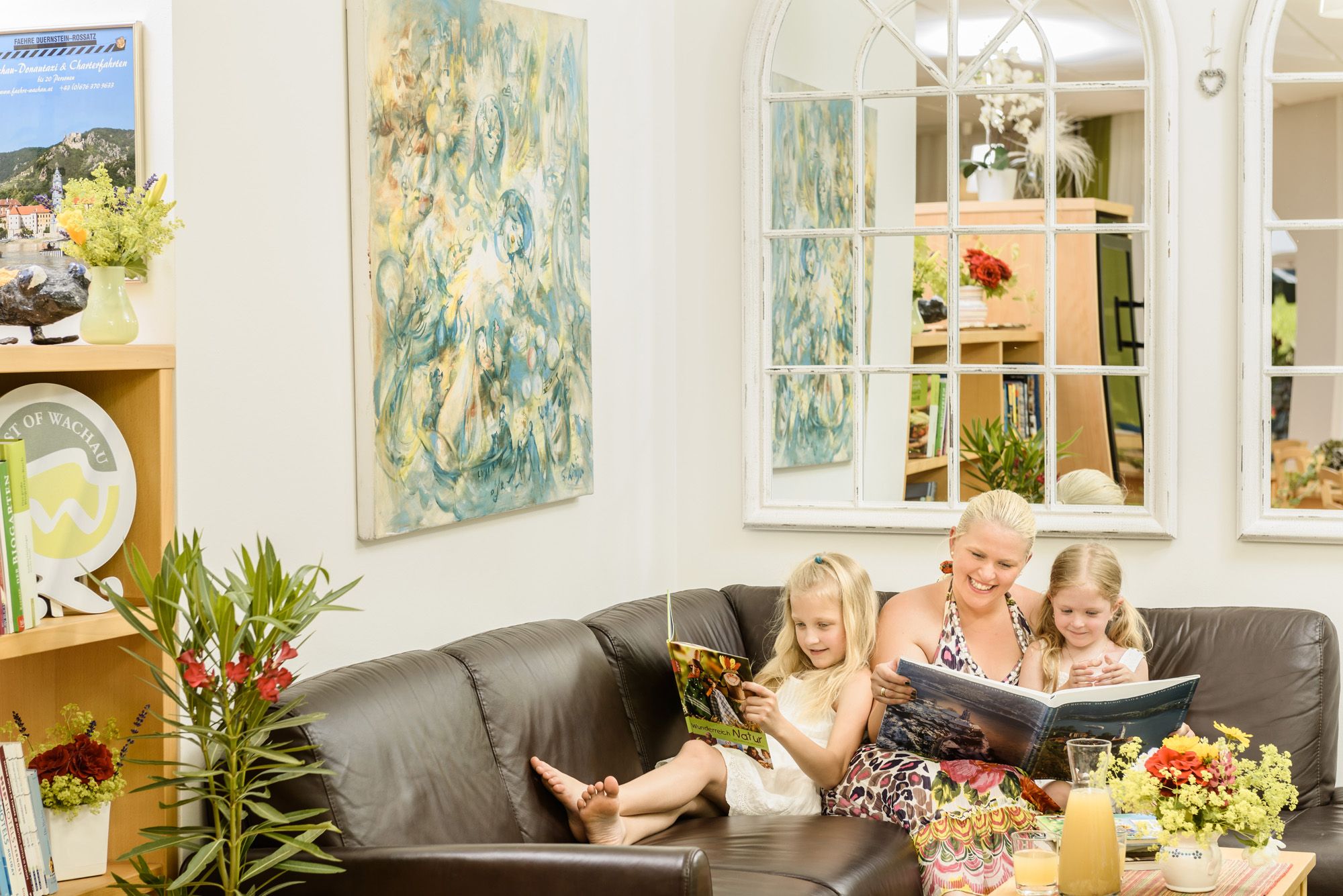 A woman and two children are reading on a sofa in a cozy room.