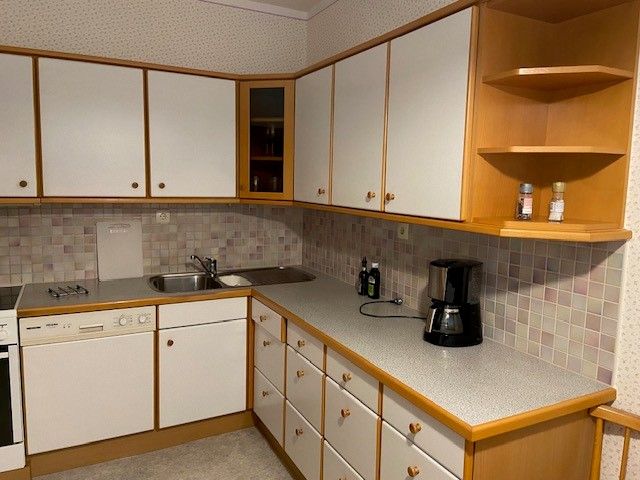 Kitchen with white cupboards, sink, coffee machine and tiled splashback.
