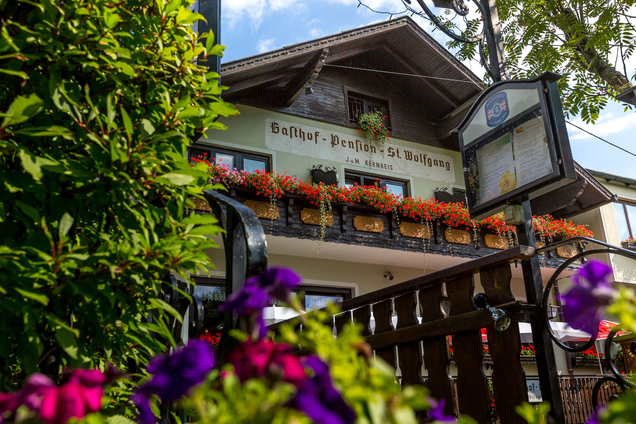 Gasthof Pension St. Wolfgang with a balcony decorated with flowers and a sign in the foreground.