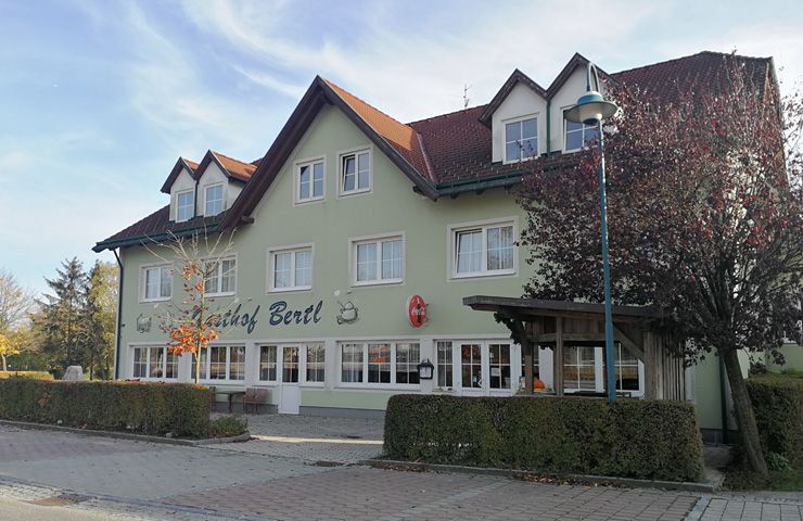 A two-storey building with the inscription 'Gasthof Bertl', surrounded by trees and bushes.