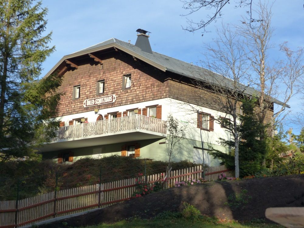 A traditional building with wooden cladding and balcony, surrounded by trees and a wooden fence. Sign: "Döhler shelter".
