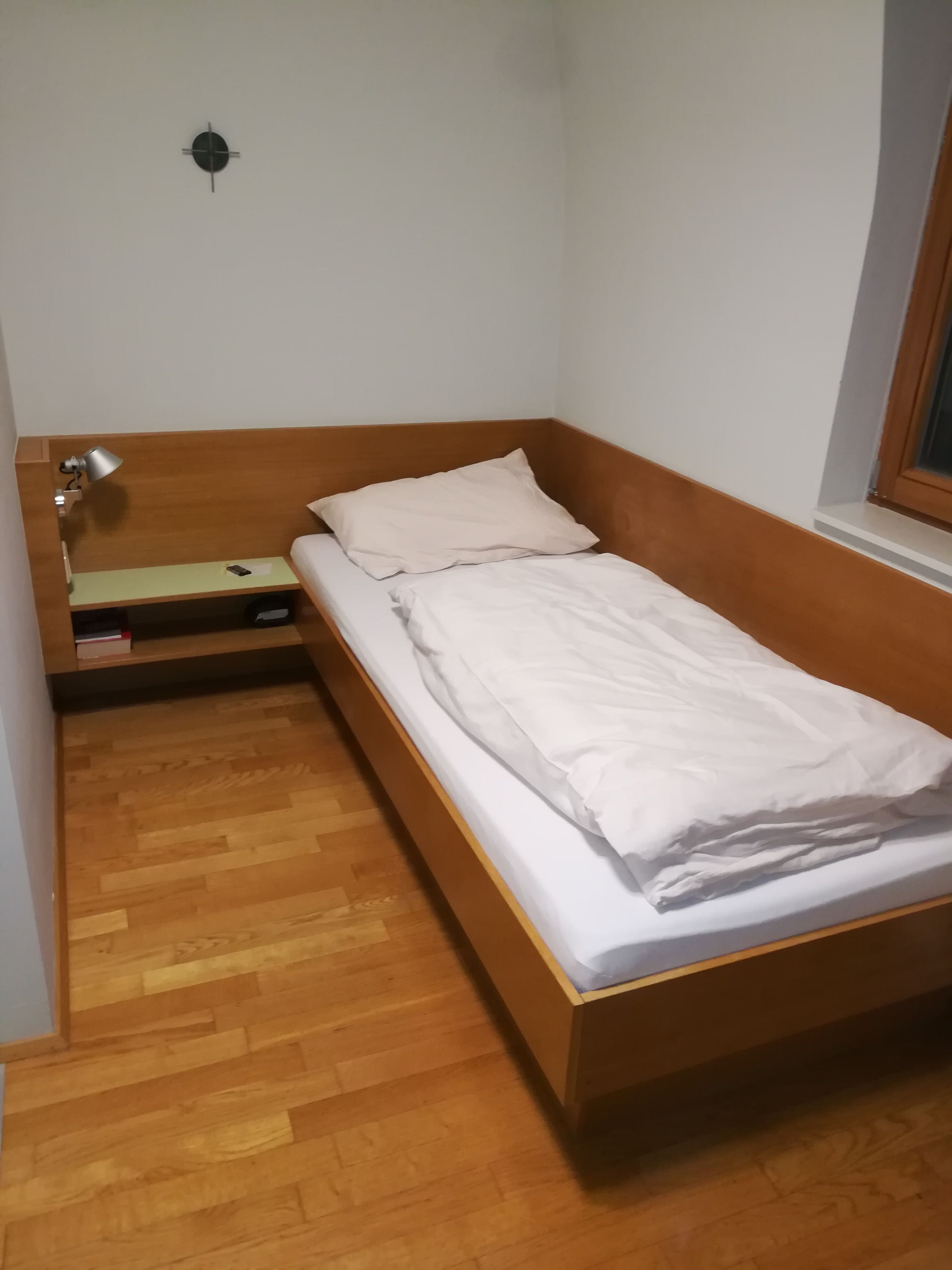 Single room with wooden bed, bedside table and lamp.