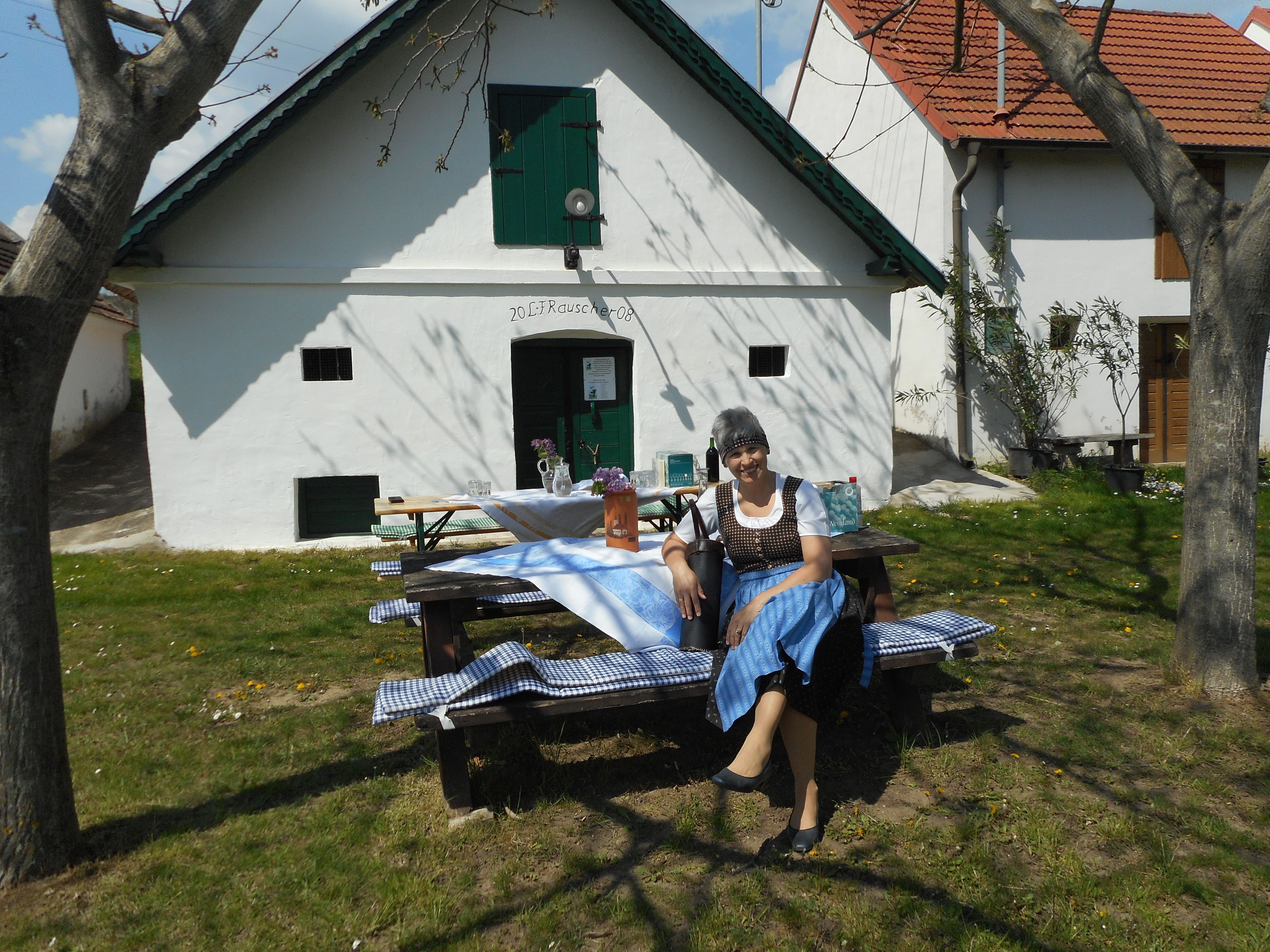 A woman in traditional dress sits on a bench in front of a white building with green shutters.