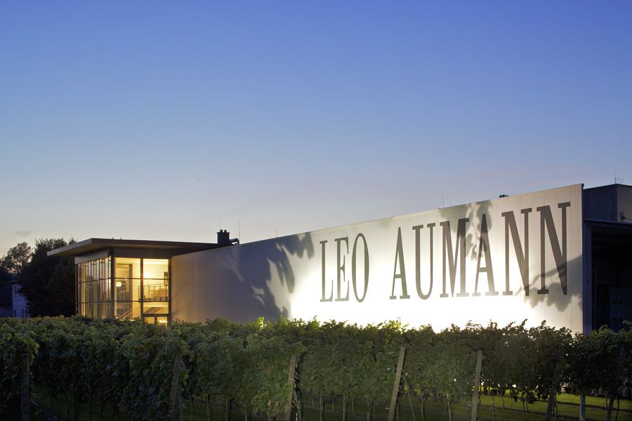 Building with the inscription 'Leo Aumann' at dusk, surrounded by vines.