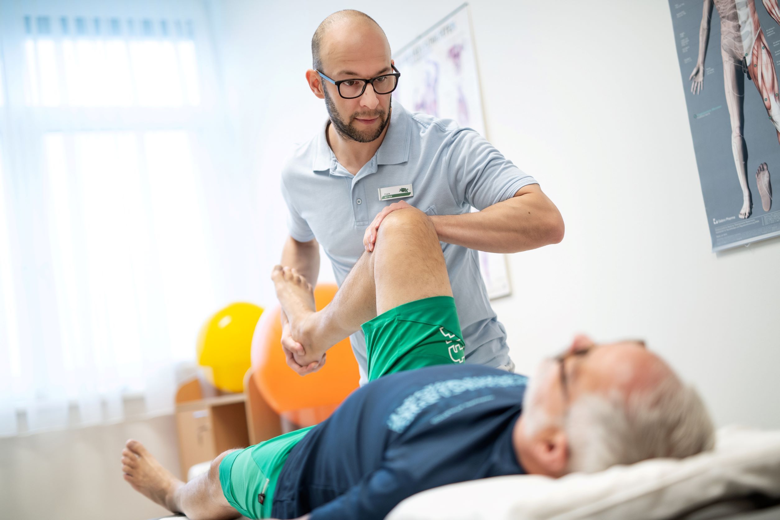 A physiotherapist treats the leg of a recumbent patient in a treatment room.