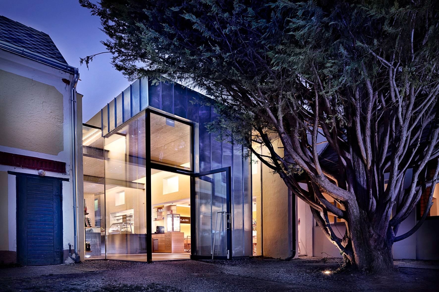 Modern glass facade of a building at night, surrounded by trees.
