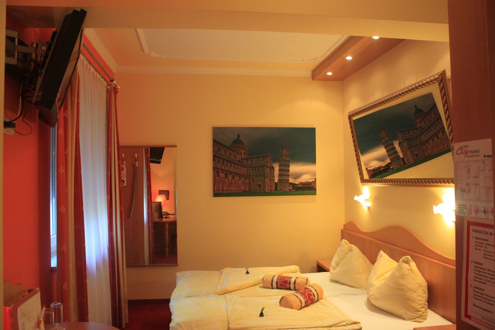 Hotel room with a double bed, pictures of the Leaning Tower of Pisa and a TV on the wall.
