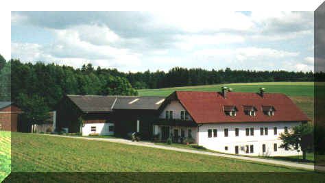 A traditional farmhouse with red roofs in a rural setting, surrounded by green fields and forests.