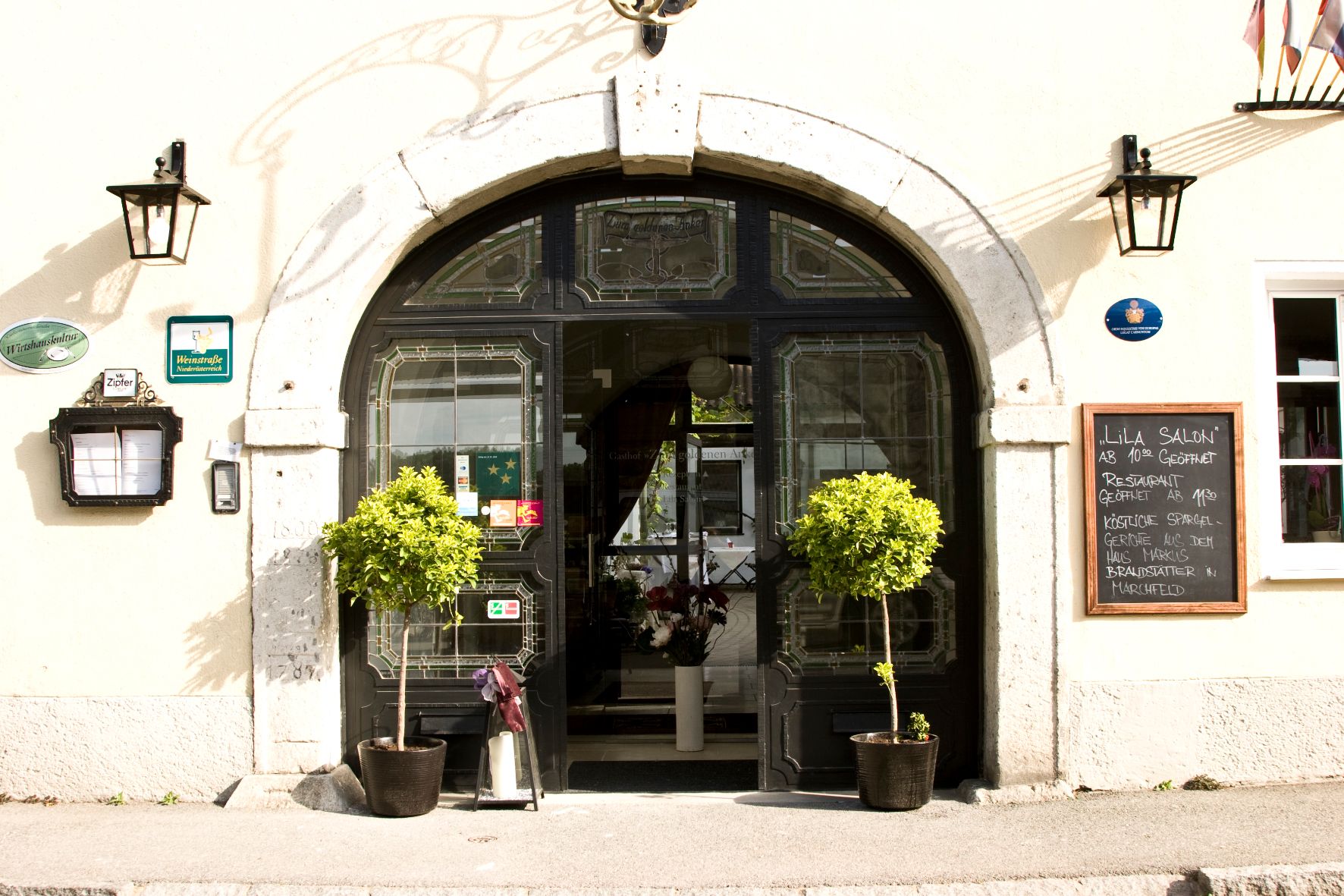 Entrance to a restaurant with decorative plants and a menu board.