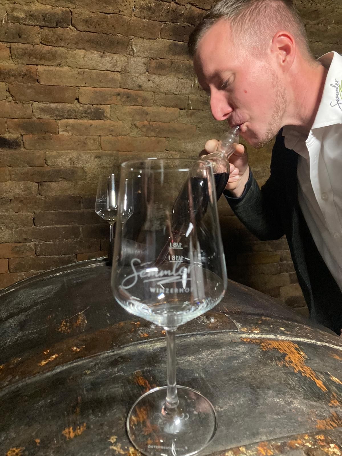A man tastes wine from a pipette in a wine cellar.