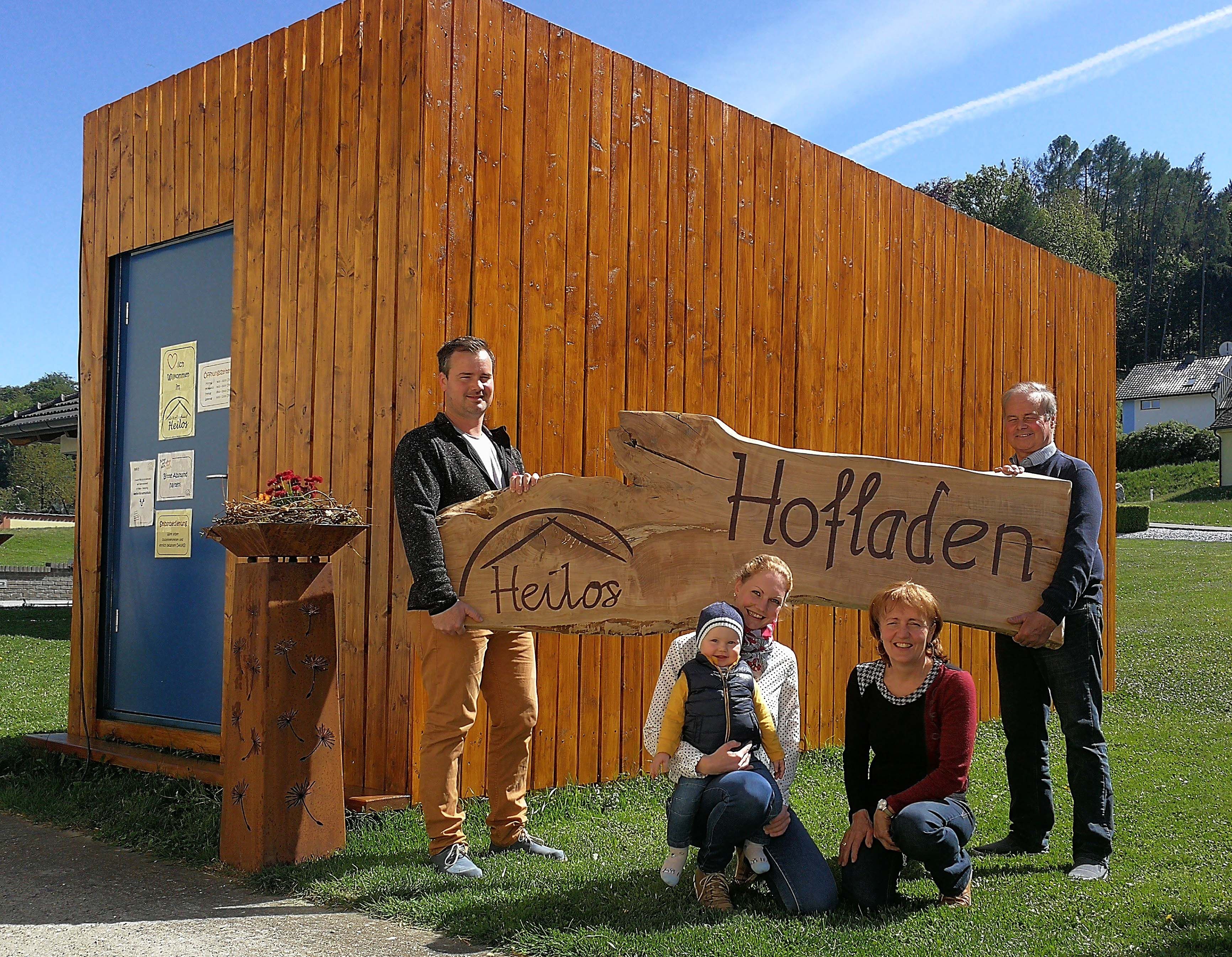 Family in front of a wooden building with a sign 'Heilos Hofladen'.