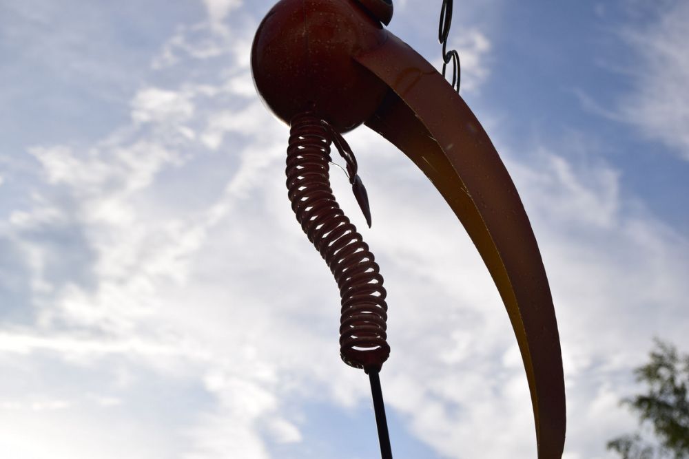 A close-up of a metal sculpture with a spiral-shaped element against a cloudy sky.