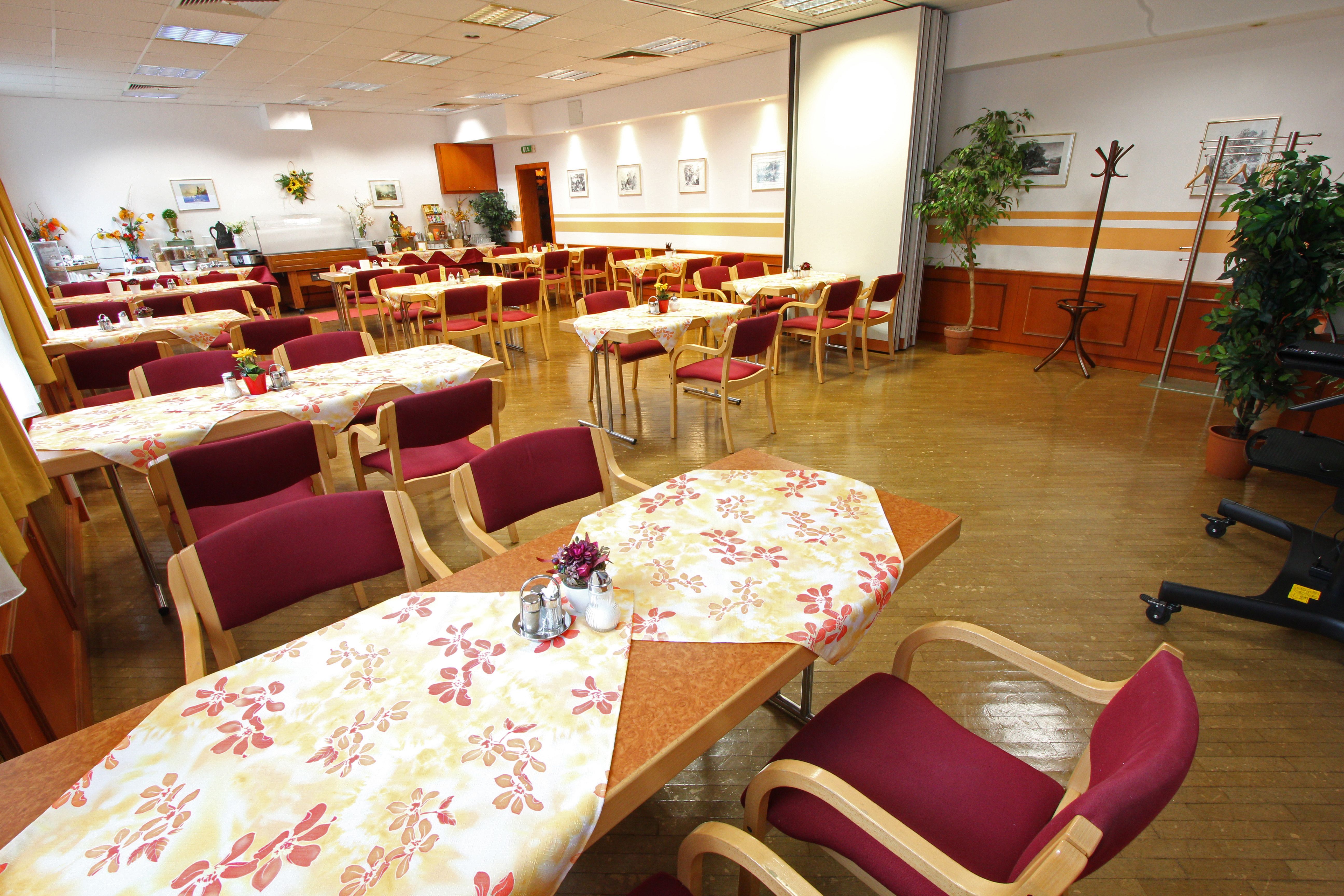 An empty dining room with laid tables and red chairs.