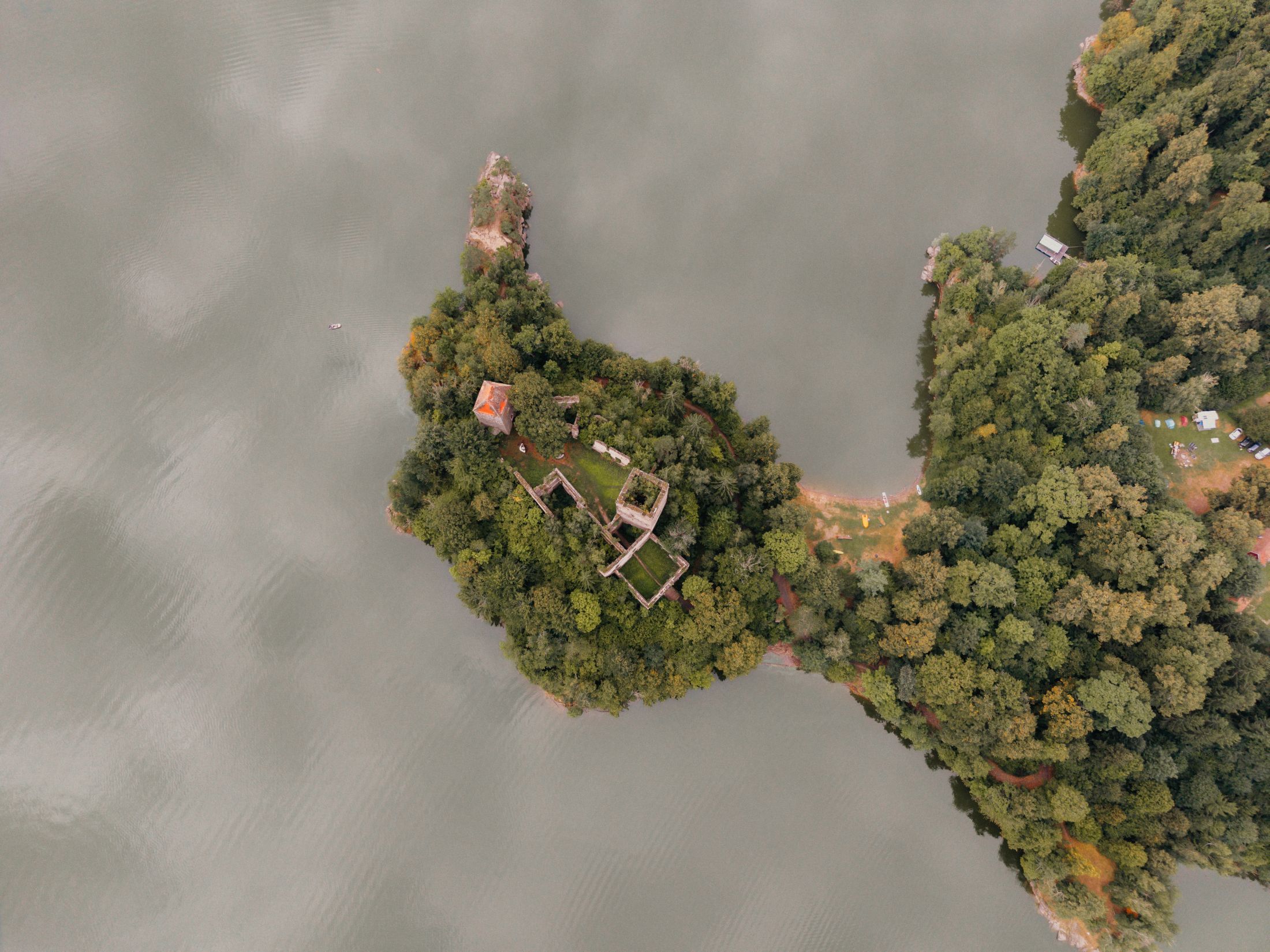 Aerial view of a wooded island with ruins and a small building on the shore of a lake.