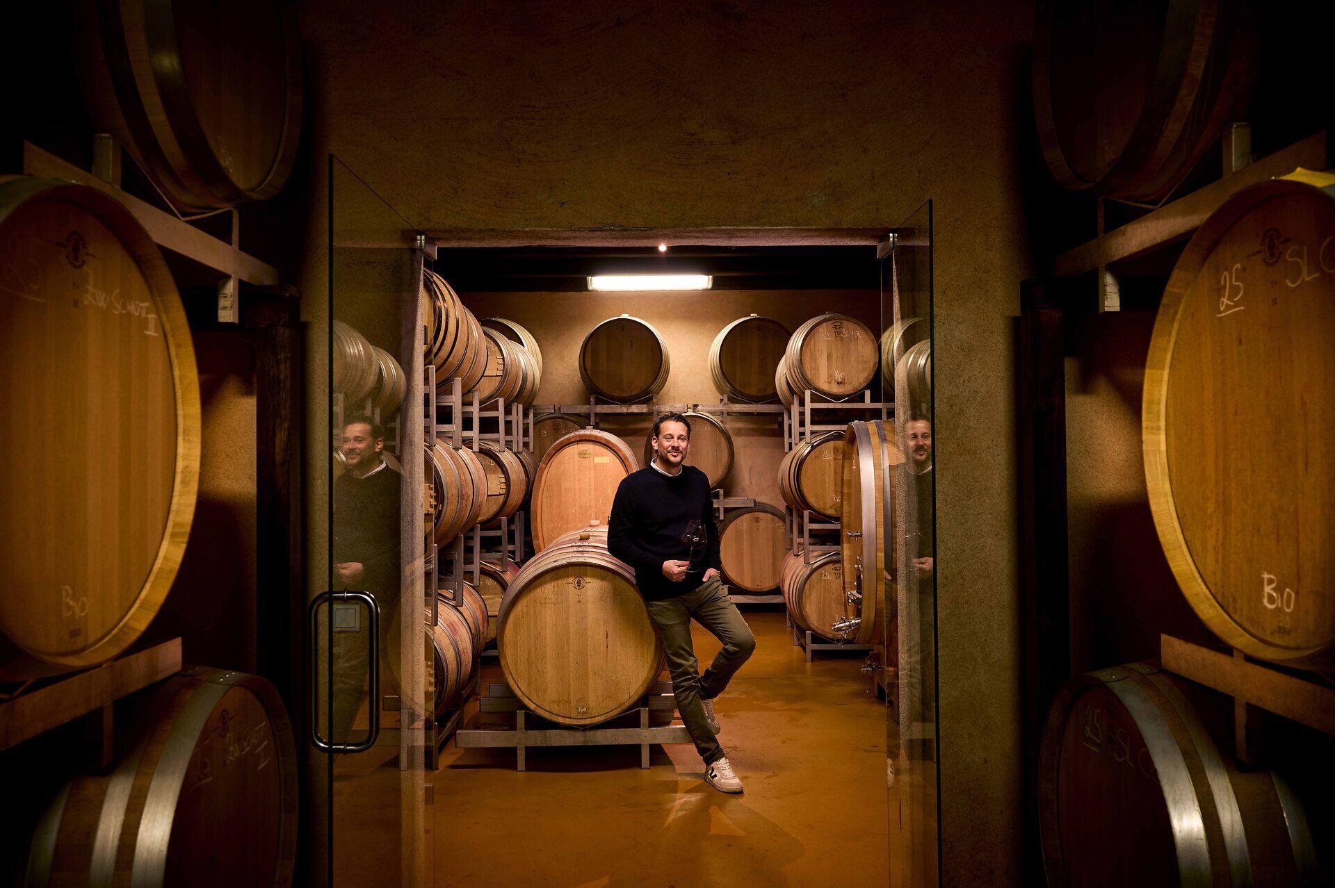 Philipp Grassl is standing in his wine cellar, leaning against a wooden barrel.