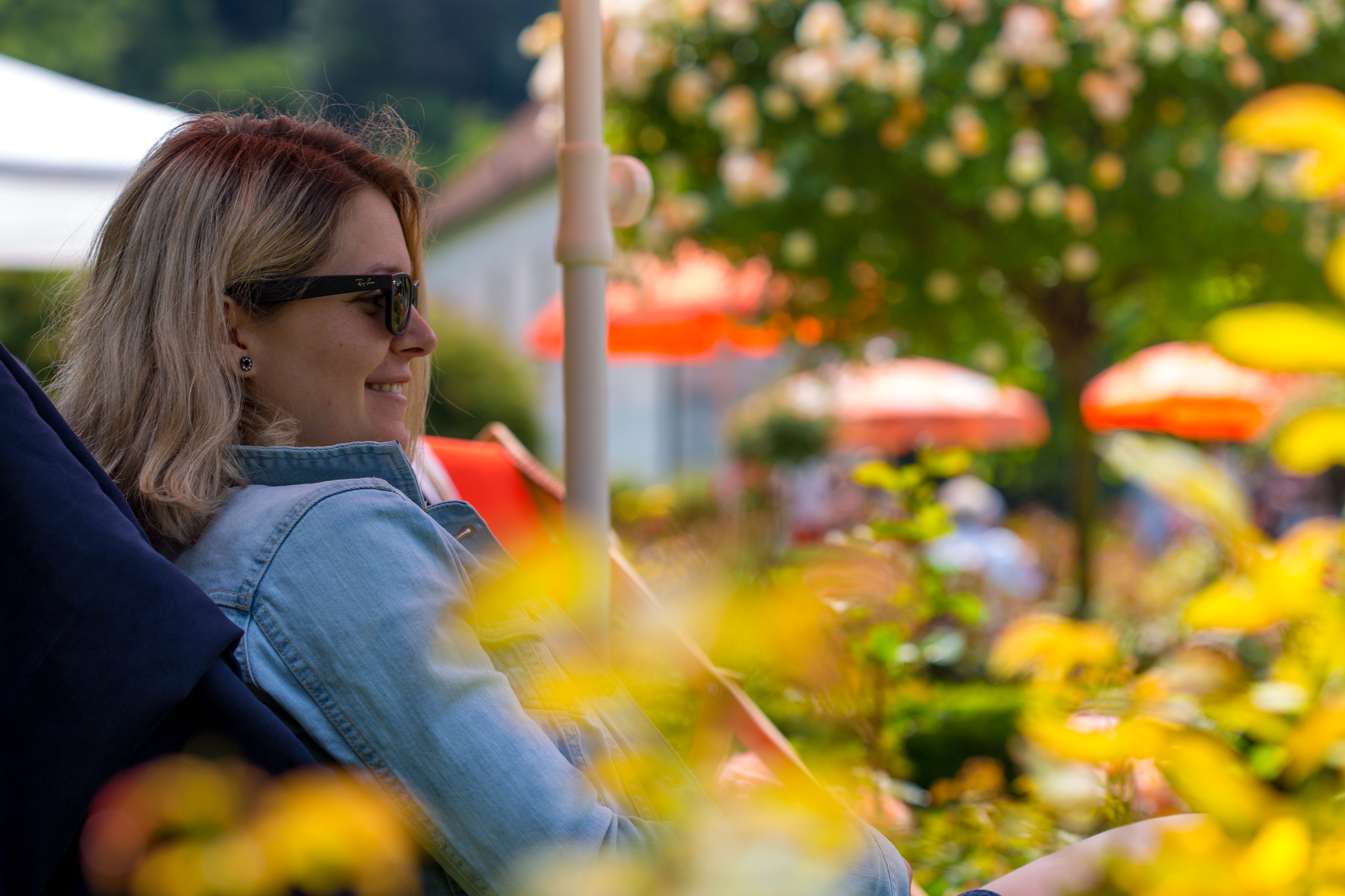 A woman lies on a deckchair under a parasol in the rose garden and smiles.