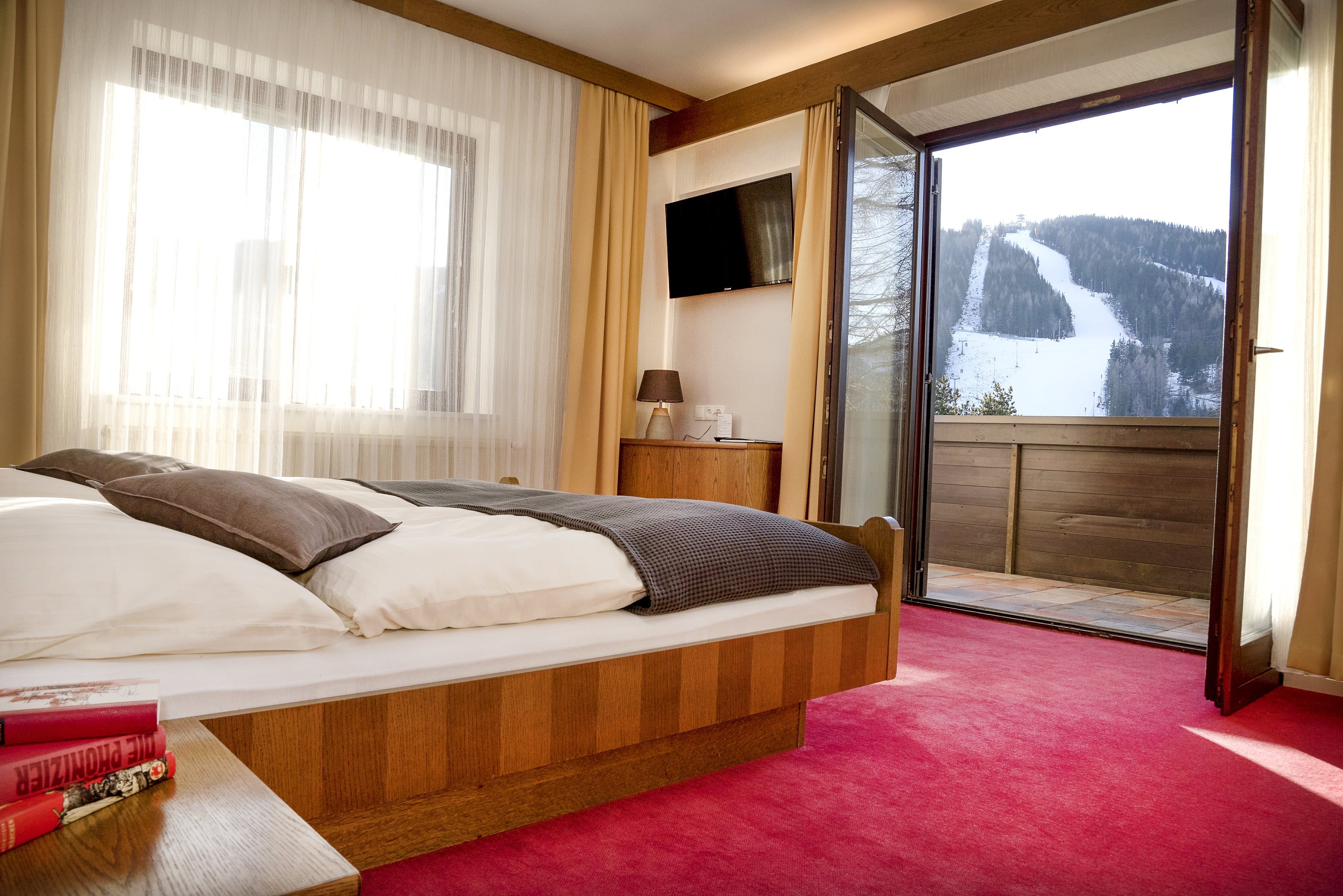 Hotel room with open balcony and view of a snow-covered ski slope.