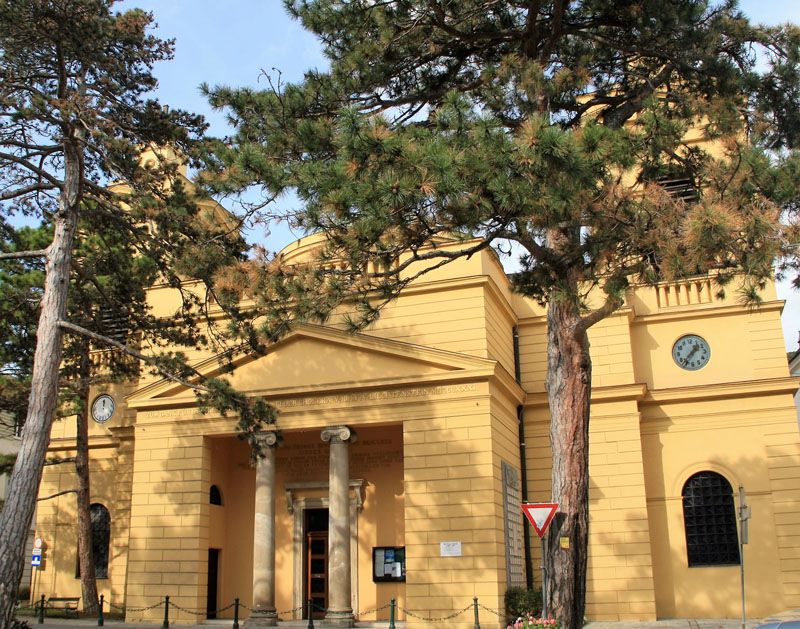 Exterior view of the Hinterbrühl parish with yellow façade and clock.