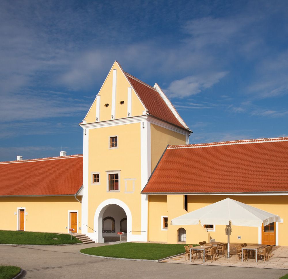 Yellow building with red roof and archway, blue sky in the background.