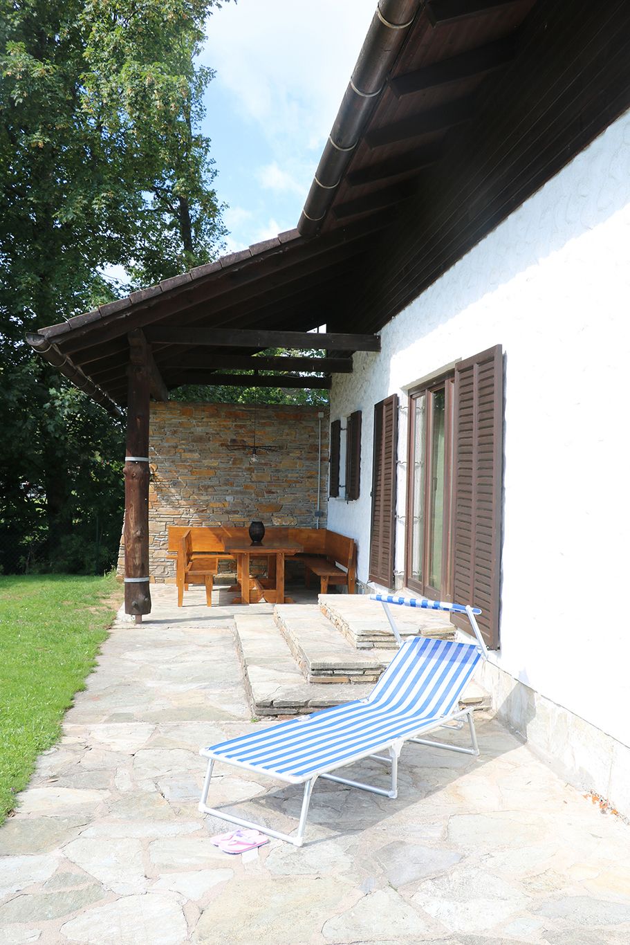 Terrace with lounger and wooden furniture next to a house with a shingle roof.