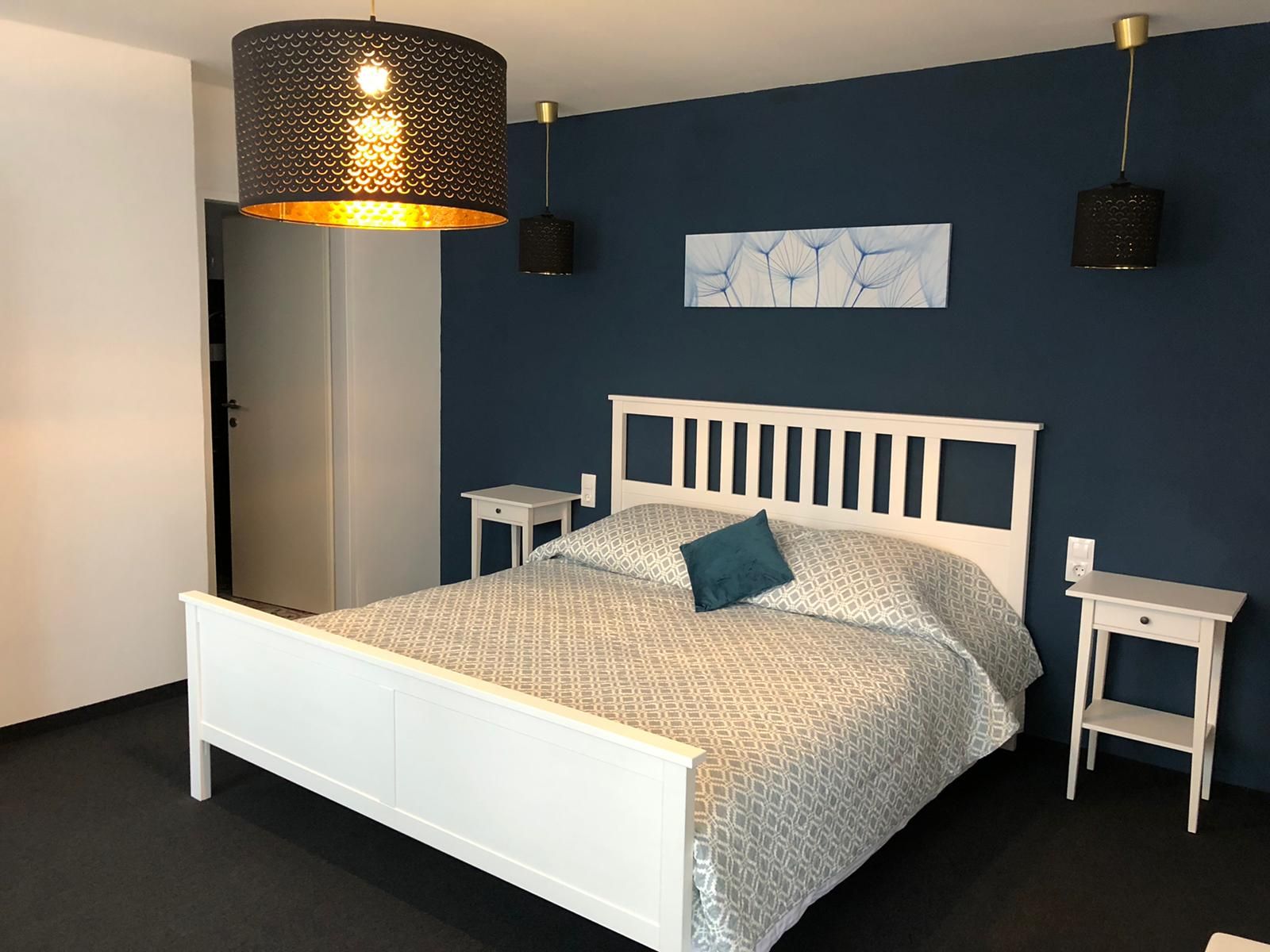 A modern double room with a white bed, blue wall and stylish lamps.