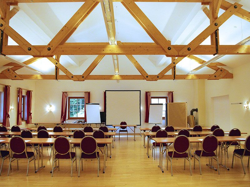 Seminar room with wooden beamed ceiling, tables and chairs, screen and flipcharts.