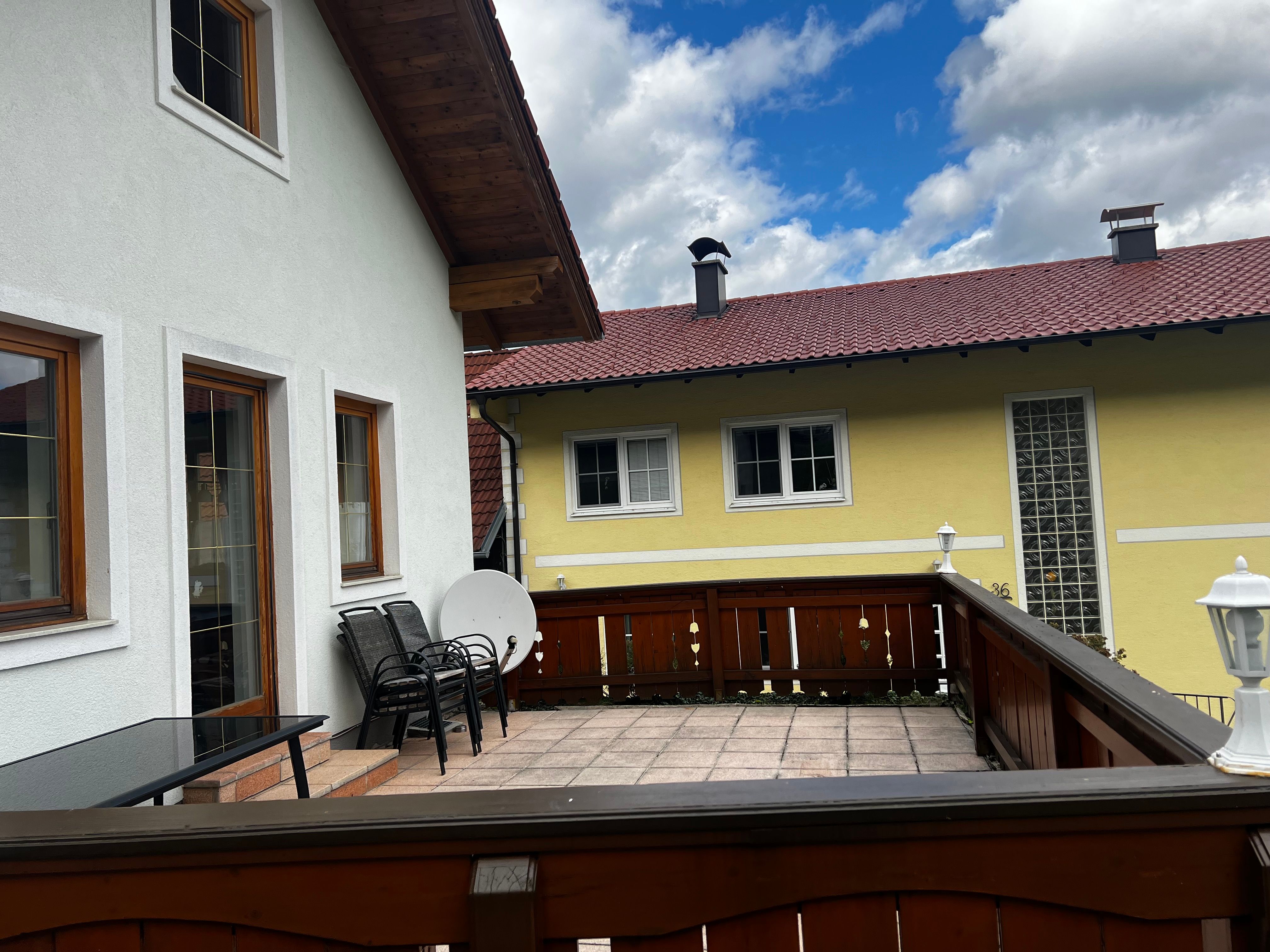 Terrace of an apartment with wooden furniture and a view of a yellow neighboring house with a red roof.