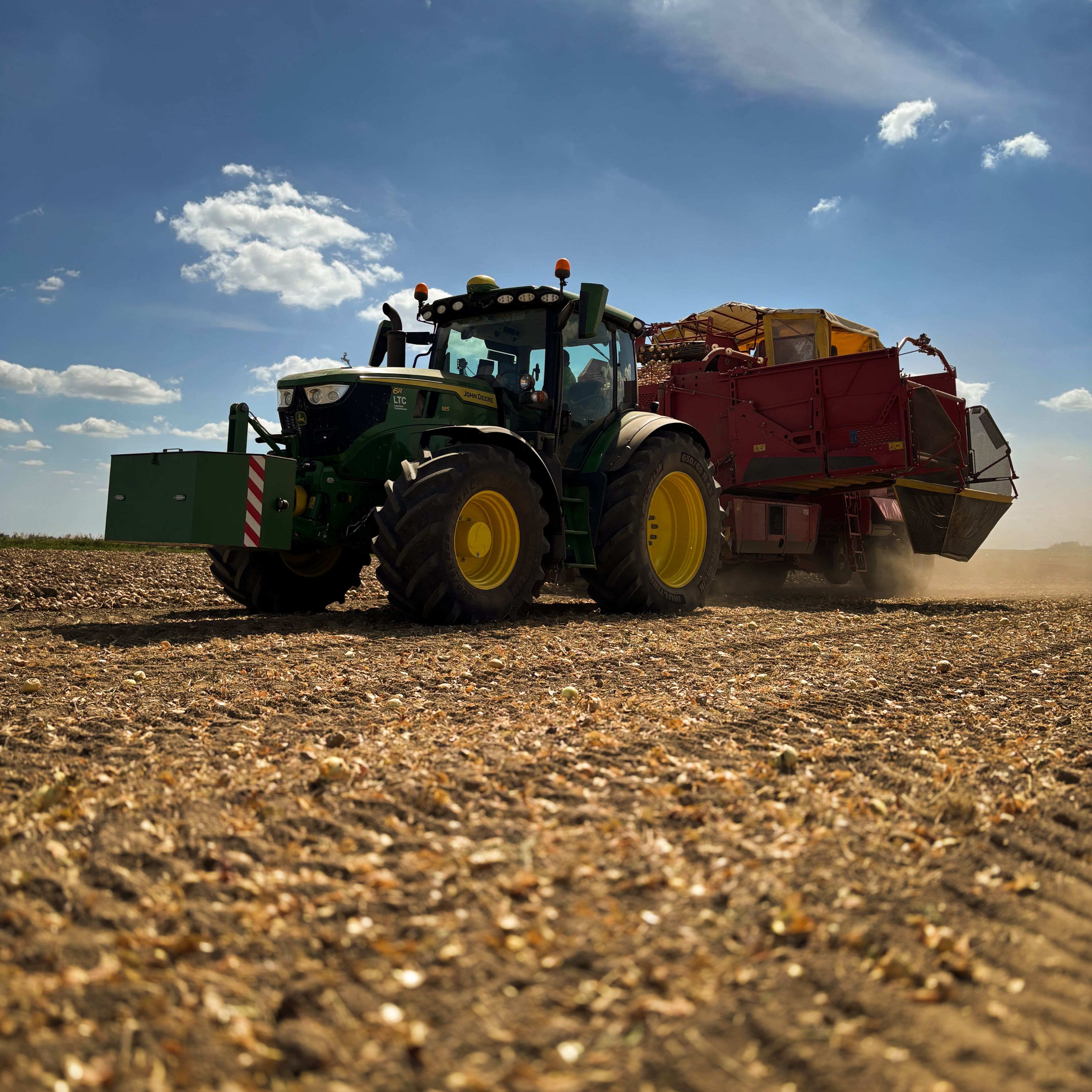A tractor with a trailer drives across a harvested field under a blue sky with a few clouds.
