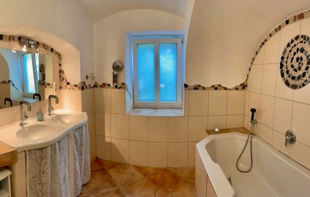 A bathroom with double washbasin, bathtub and tiled floor.