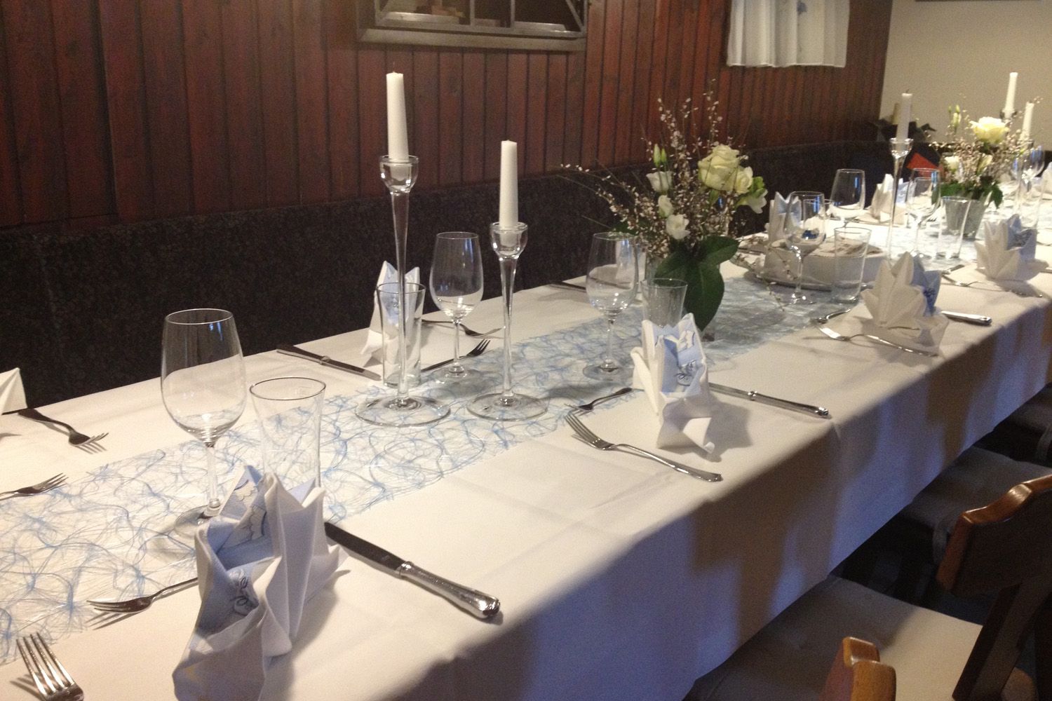 Elegant, festively laid table with white tablecloths, candles and flower arrangements.