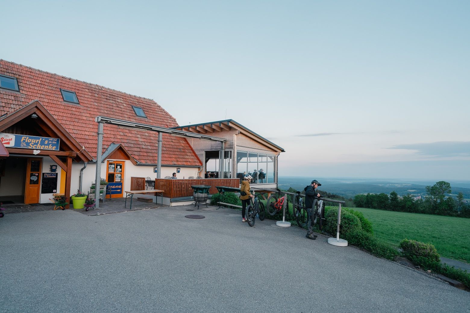 An inn with a terrace and cyclists in a rural setting.