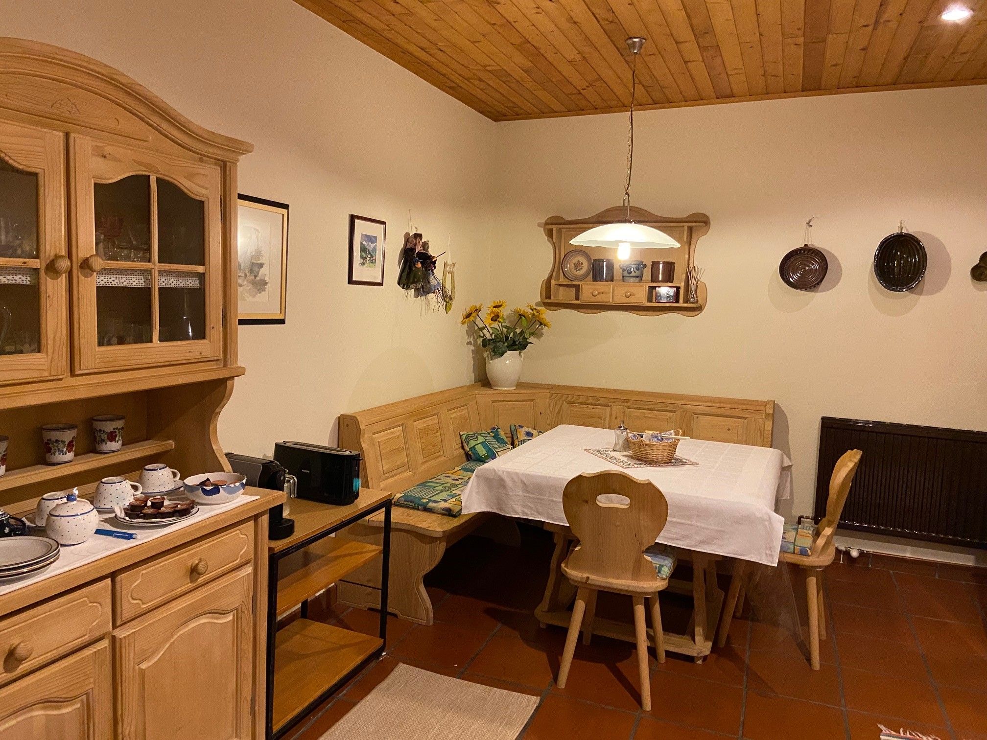Cozy kitchen with wooden furniture, dining table and corner bench, decorated with crockery and flowers.