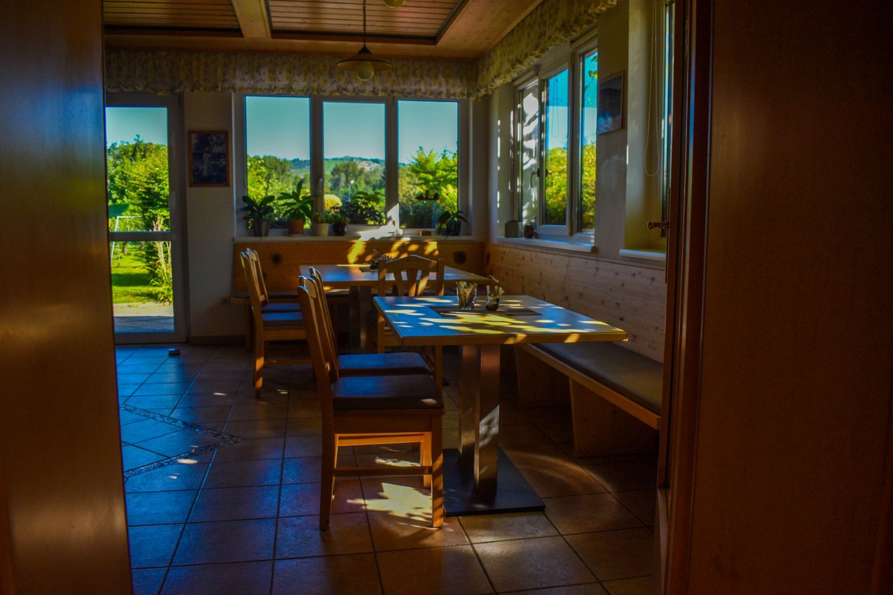 A cozy breakfast room with wooden furniture and large windows that let in sunlight.