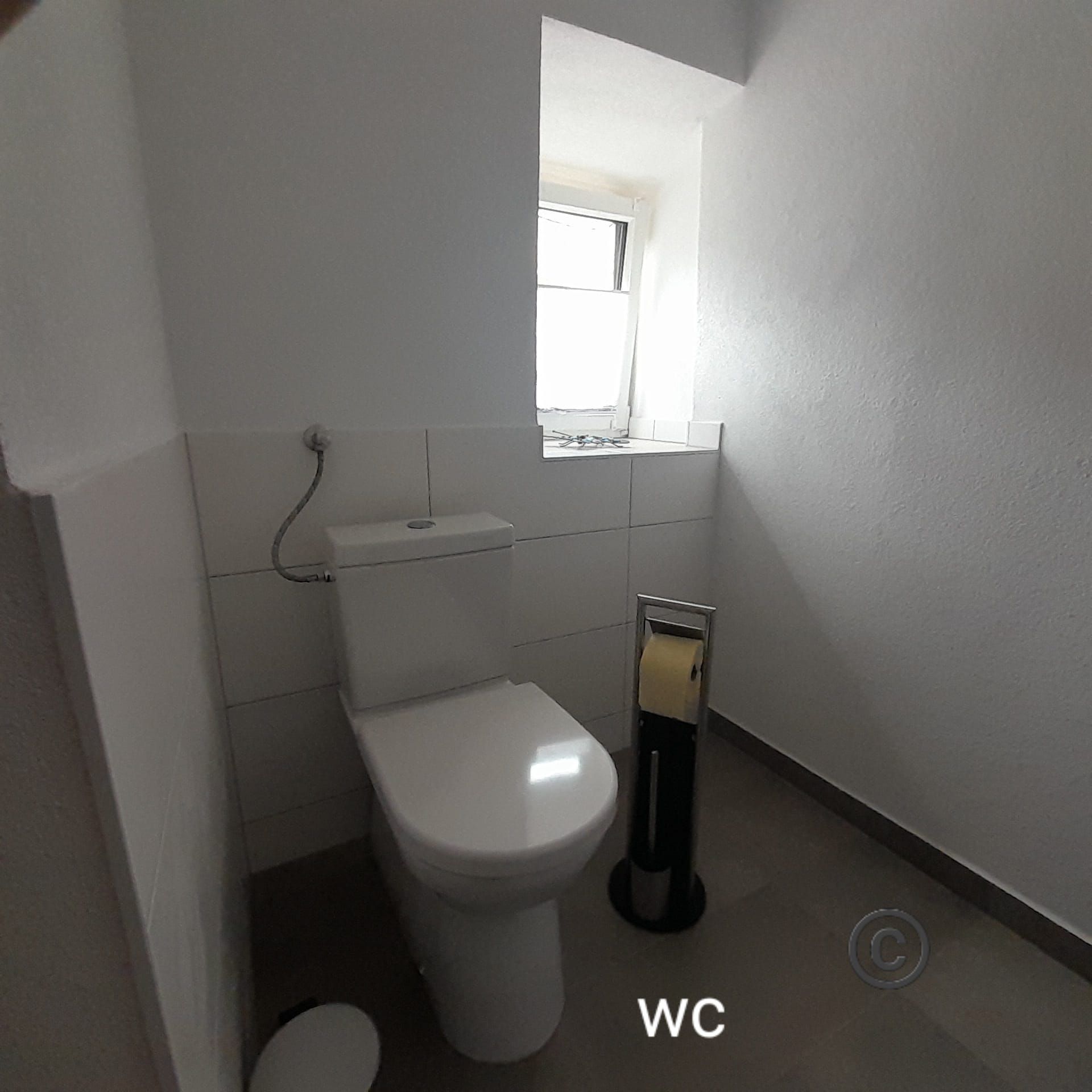 A simple bathroom with toilet, toilet paper holder and small window.