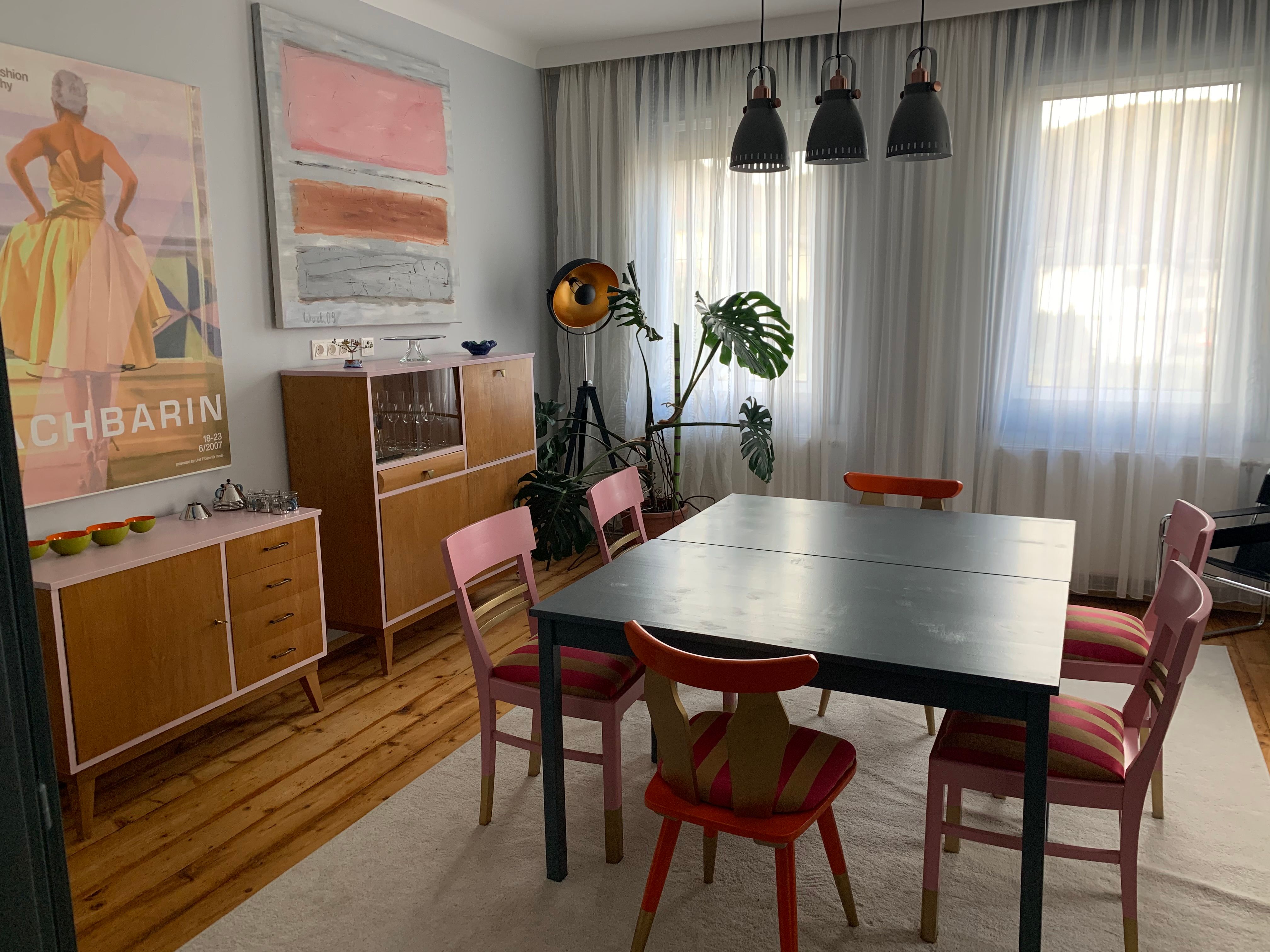Dining area with table, chairs, chests of drawers and works of art on the wall.