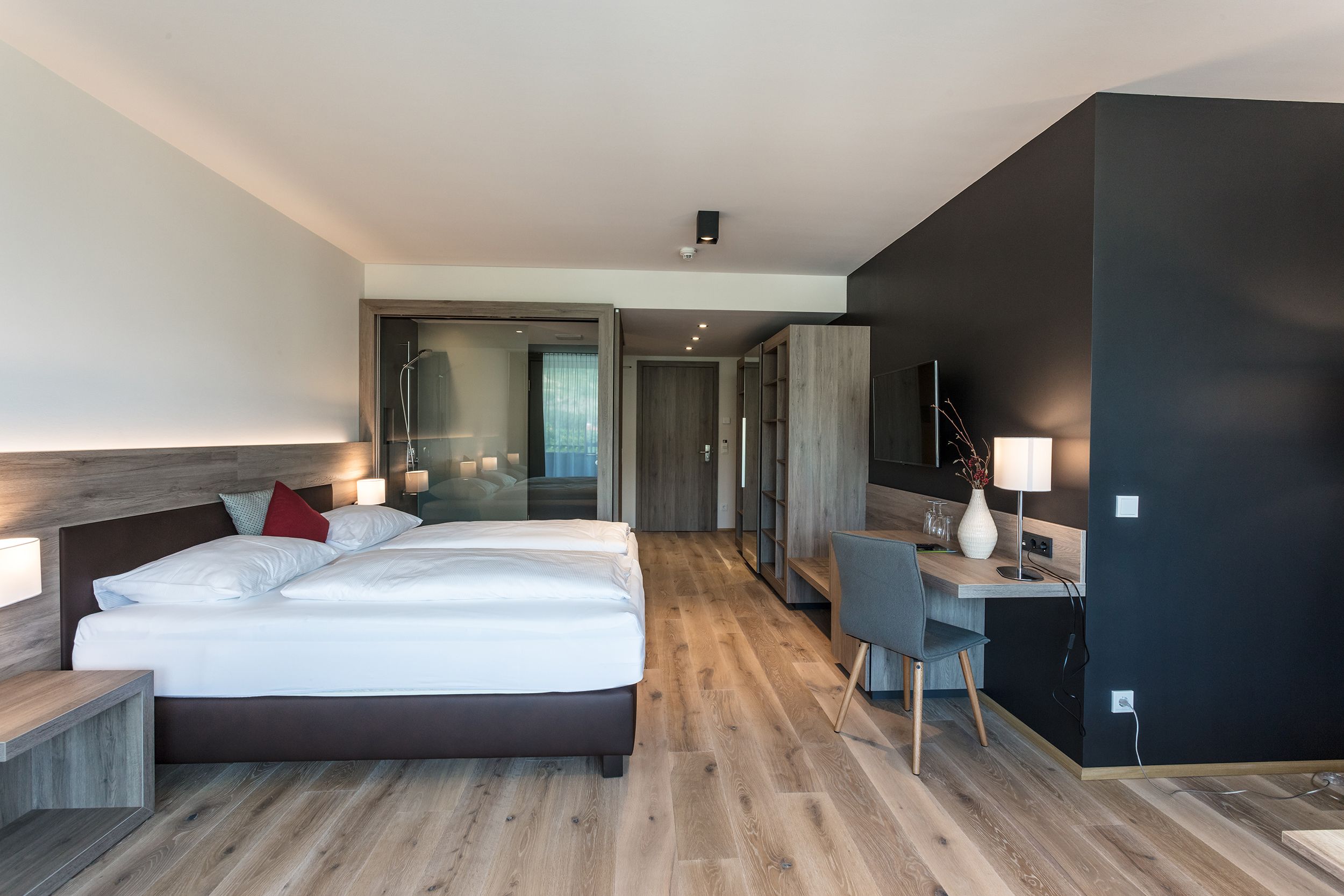 Modern hotel room with double bed, desk and wooden floor.