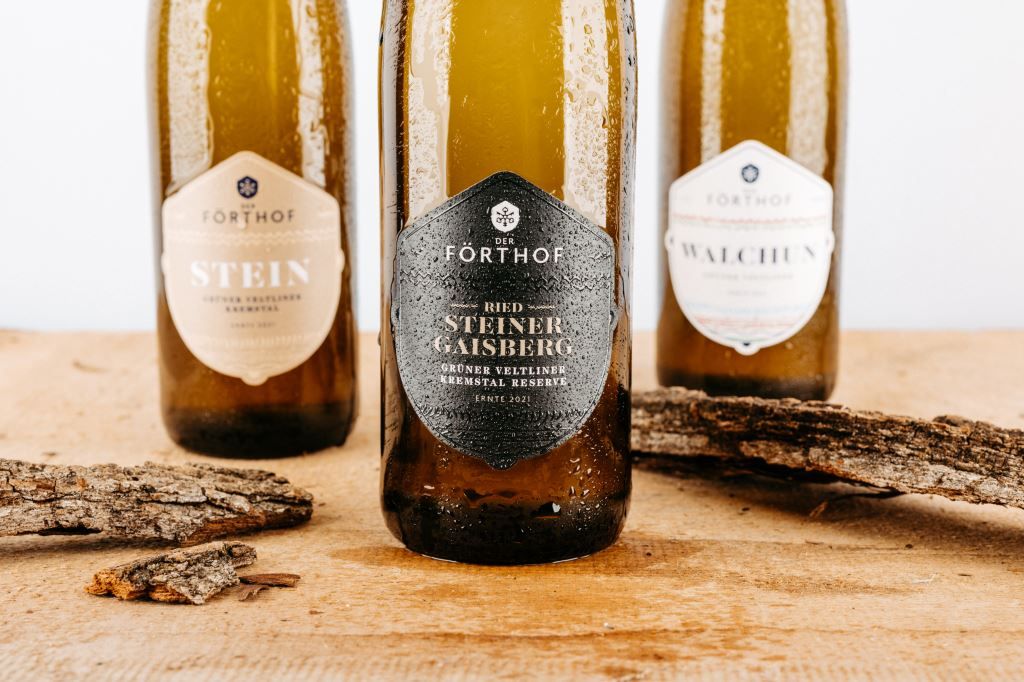 Three Förthof wine bottles on a wooden table with pieces of bark.
