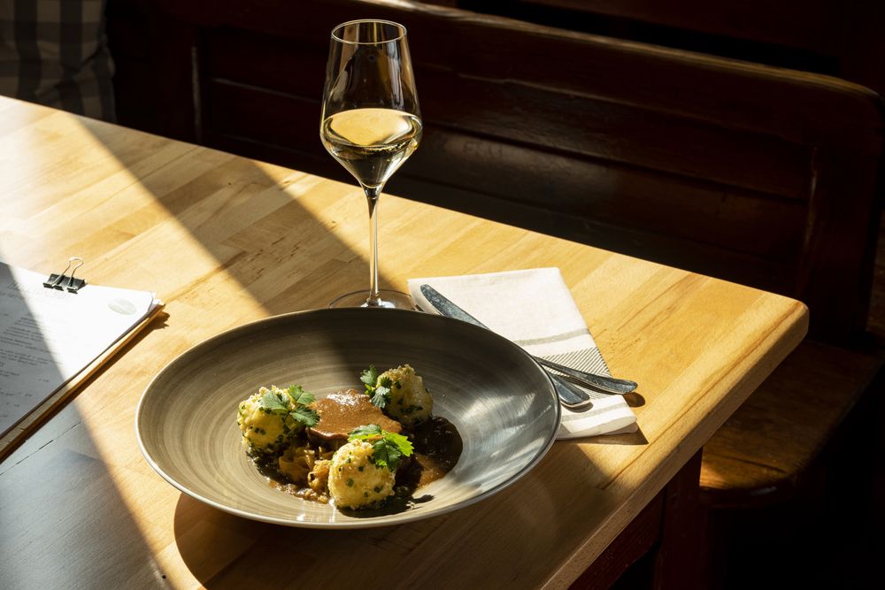 Plate with meat, dumplings and sauce, wine glass on a wooden table in the sunlight.