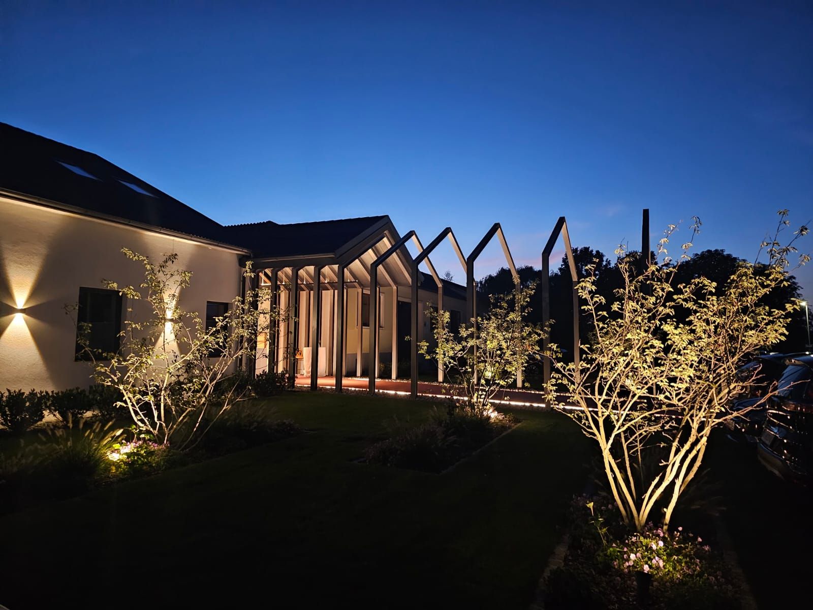 Illuminated building at night with modern structures and trees in the foreground.