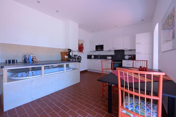 Modern kitchen with white cupboards, dining table and red chairs.