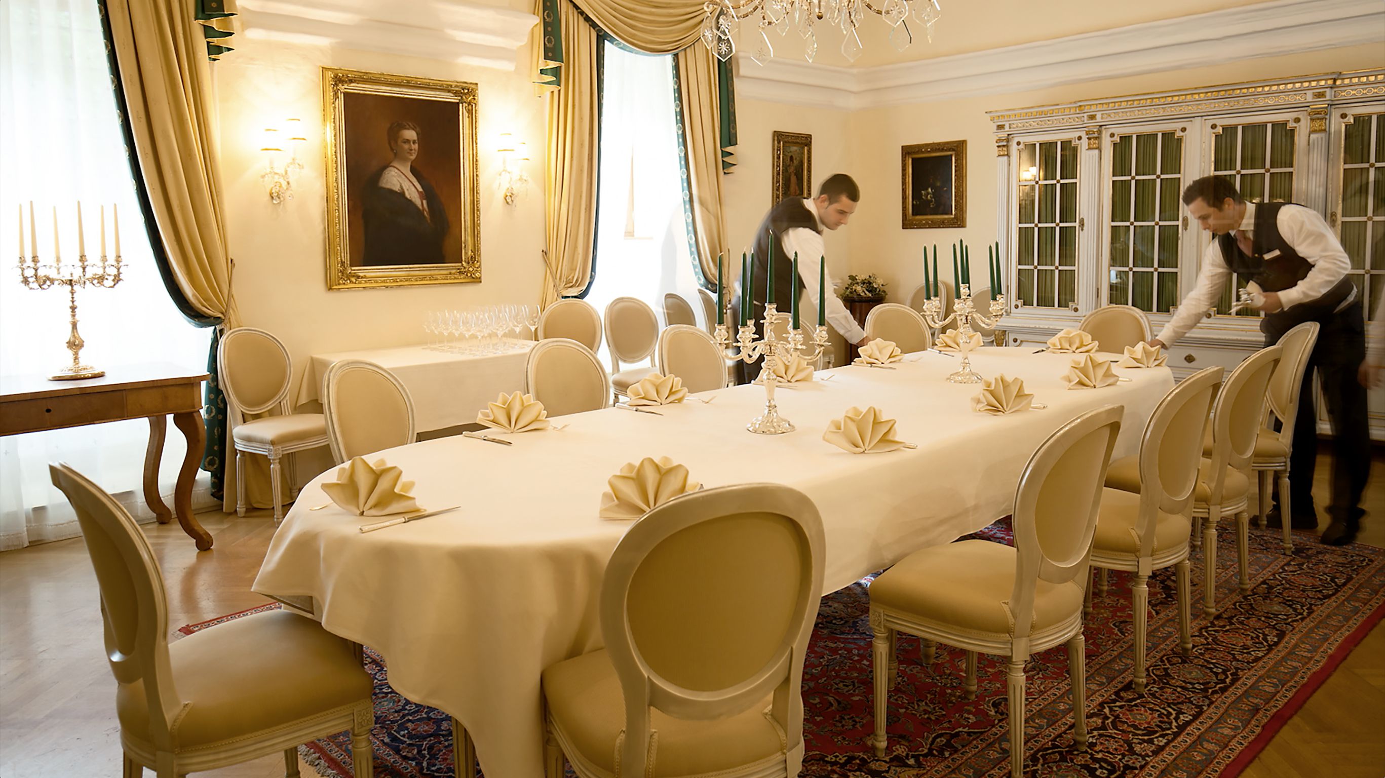 Elegant dining room with laid table, candlesticks and two waiters.
