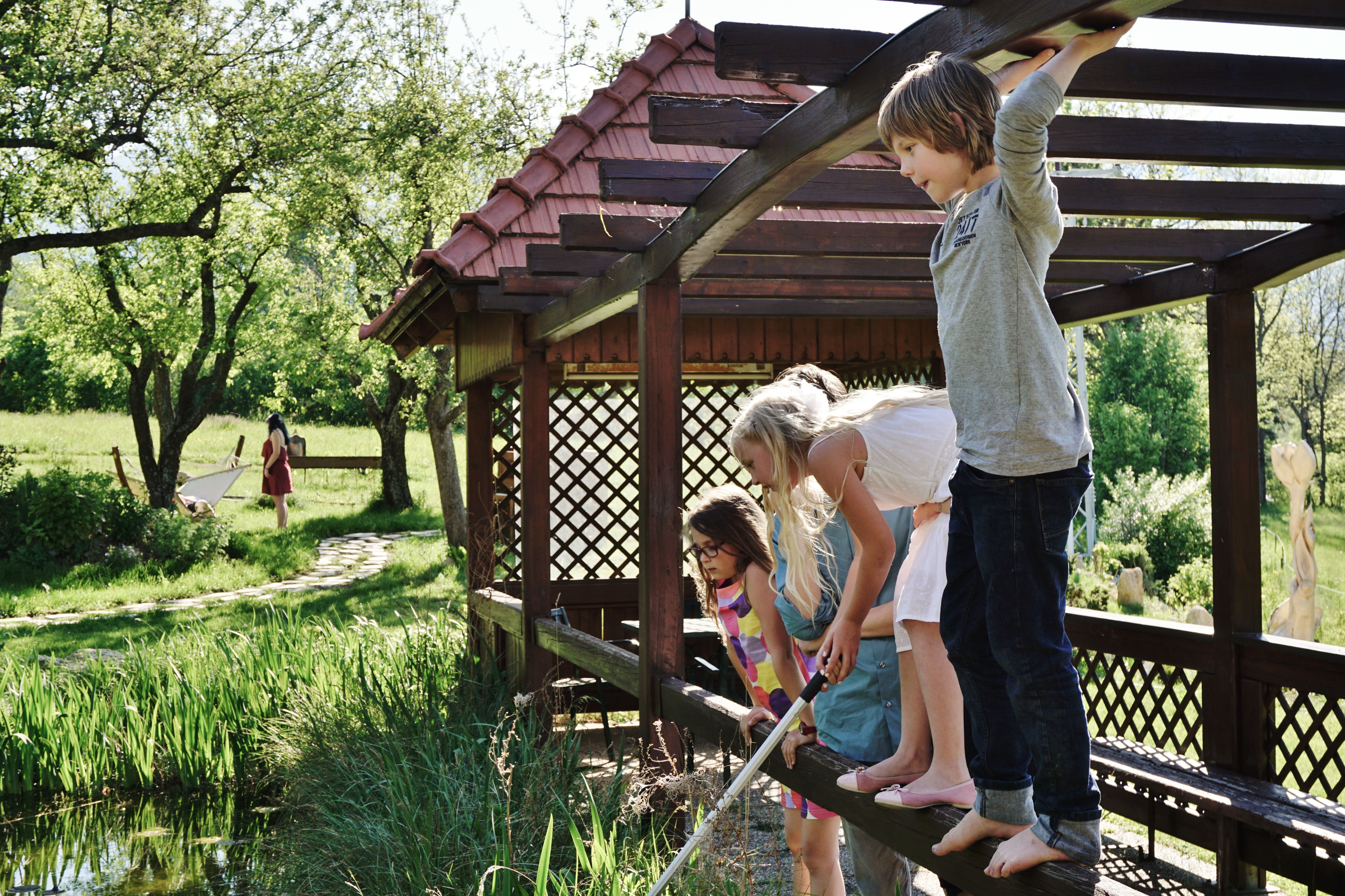Children playing on a wooden bridge over a pond in a garden.